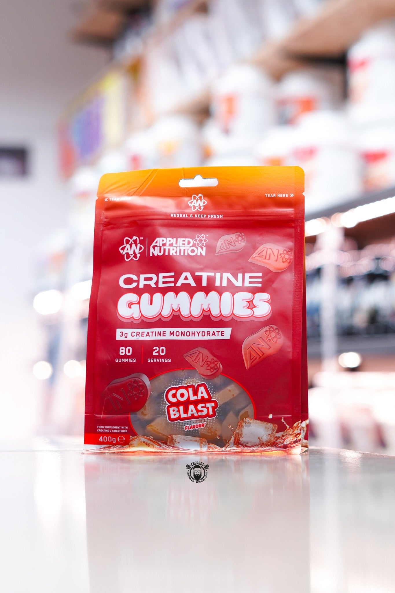 Applied Nutrition creatine gummies pouch, Cola Blast flavour, resealable bag with 3g creatine monohydrate per serving, 80 gummies (20 servings), displayed on counter in supplement store.