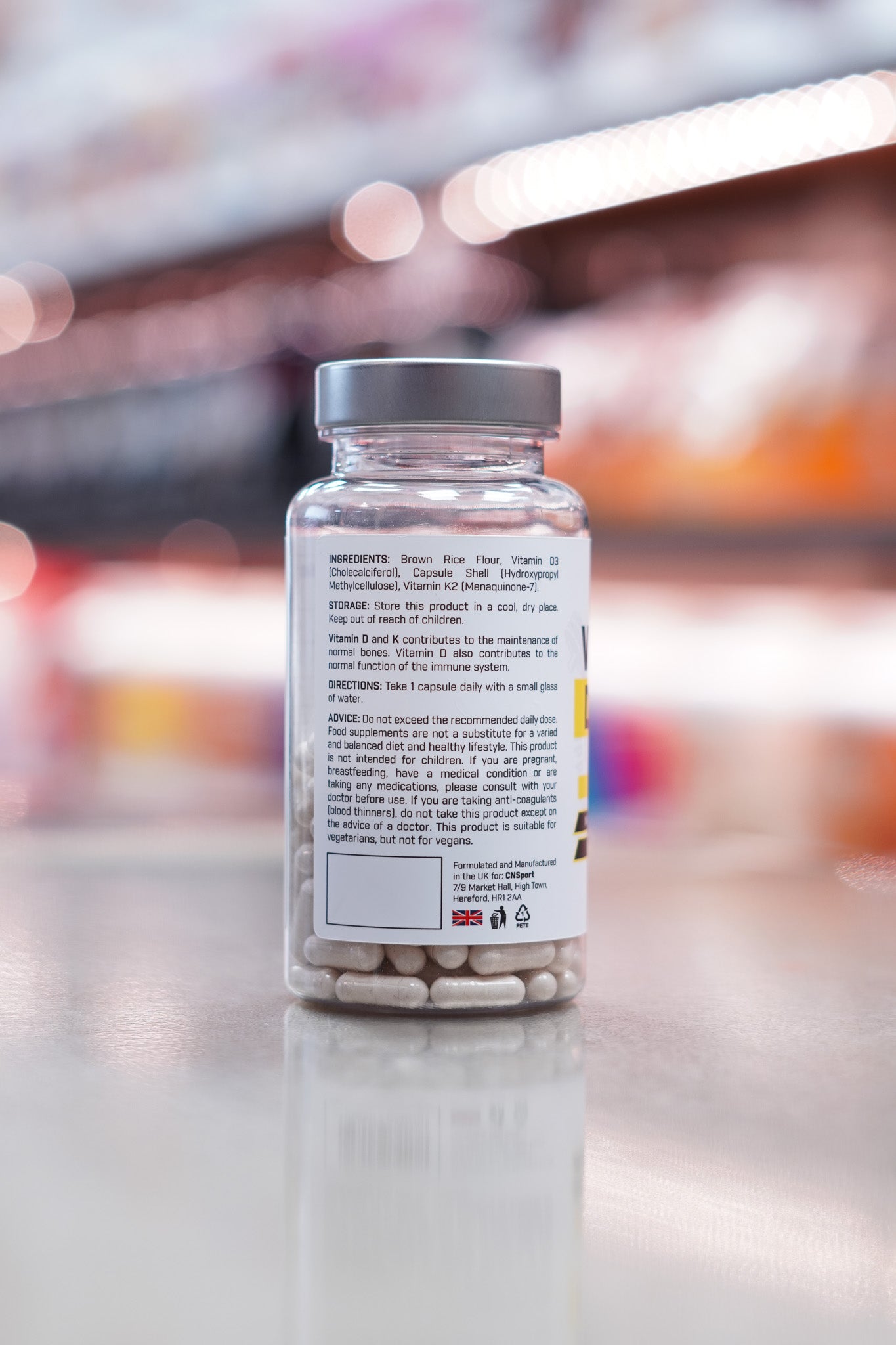 Side view of CNSport Vitamin D3 + K2 bottle showing ingredients, directions, storage instructions, and safety advice. Includes manufacturing details indicating the product is made in the UK.