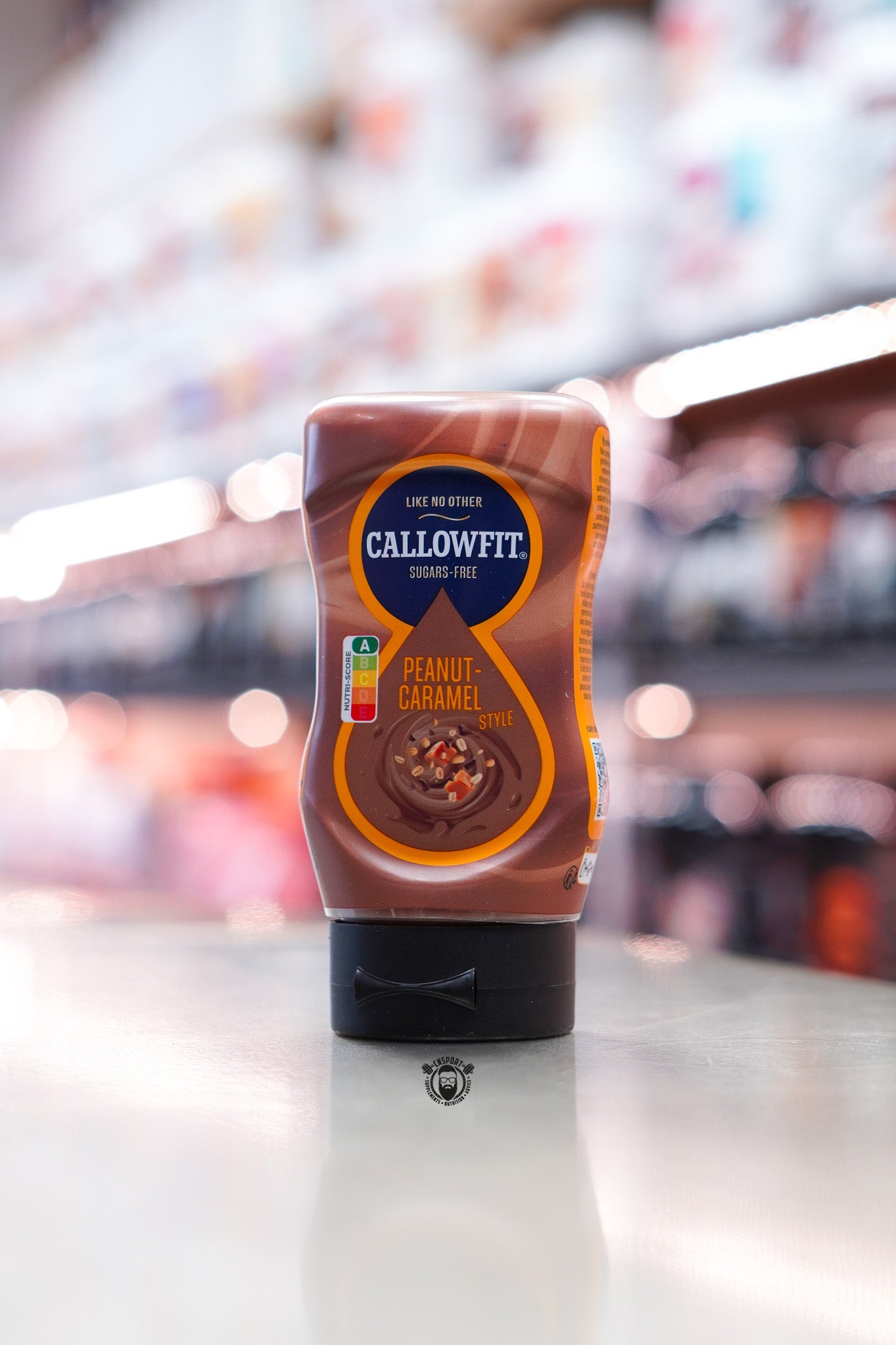 Callowfit Peanut-Caramel Style Sauce 300ml sugar-free bottle with peanut caramel flavour branding displayed on a countertop in a supplement store.