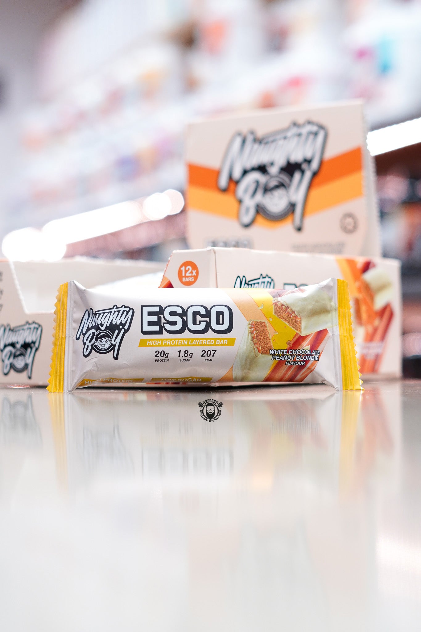 Naughty Boy ESCO high protein layered bar, White Chocolate Peanut Blondie flavour (20g protein), displayed in front of 12-bar retail box in supplement store.