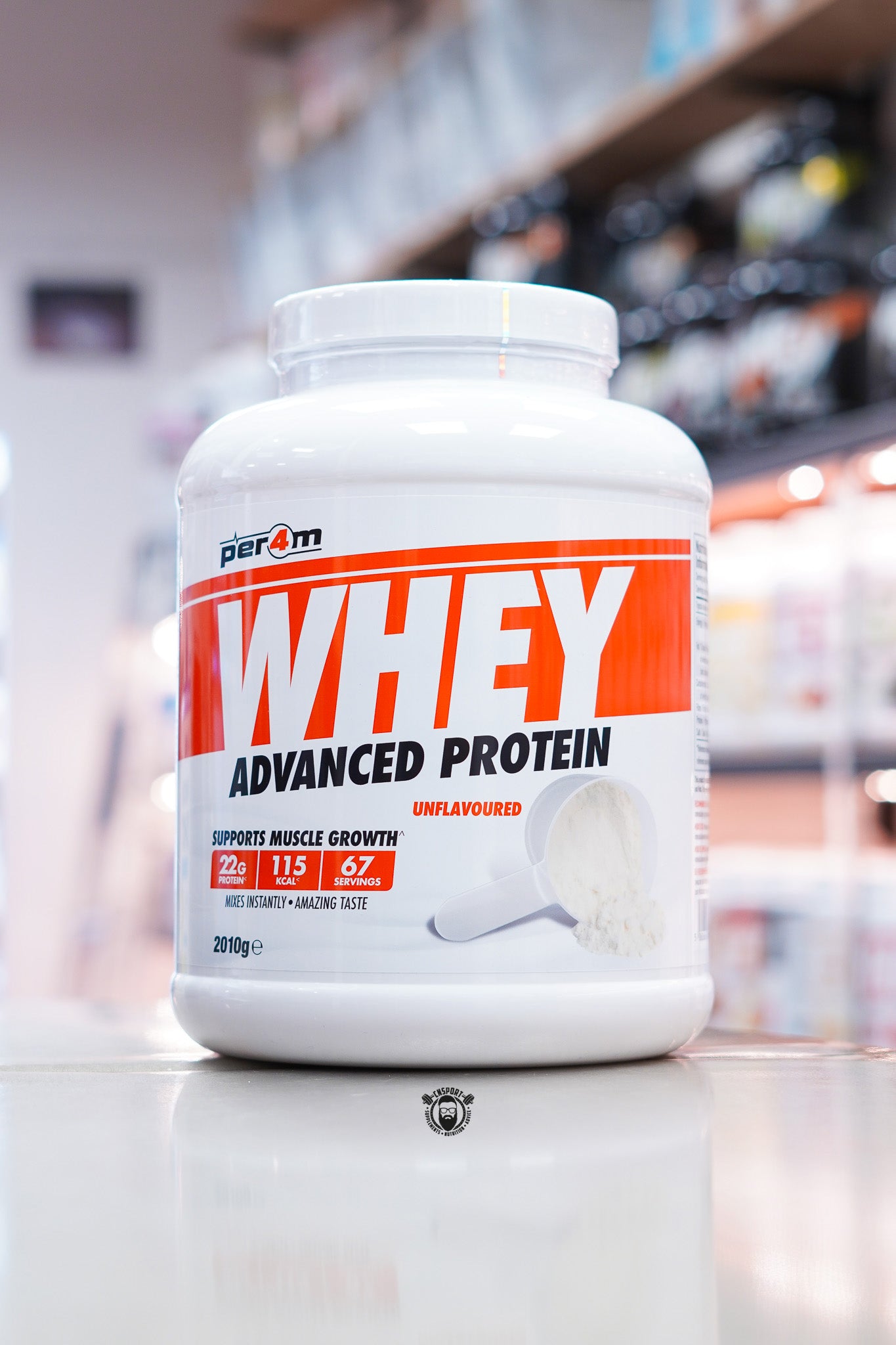 Per4m Whey Advanced Protein Unflavoured 2kg protein powder tub displayed on a countertop in a supplement store, featuring 22g protein per serving, 115 calories, 67 servings, and an unflavoured whey protein scoop graphic on the front label.