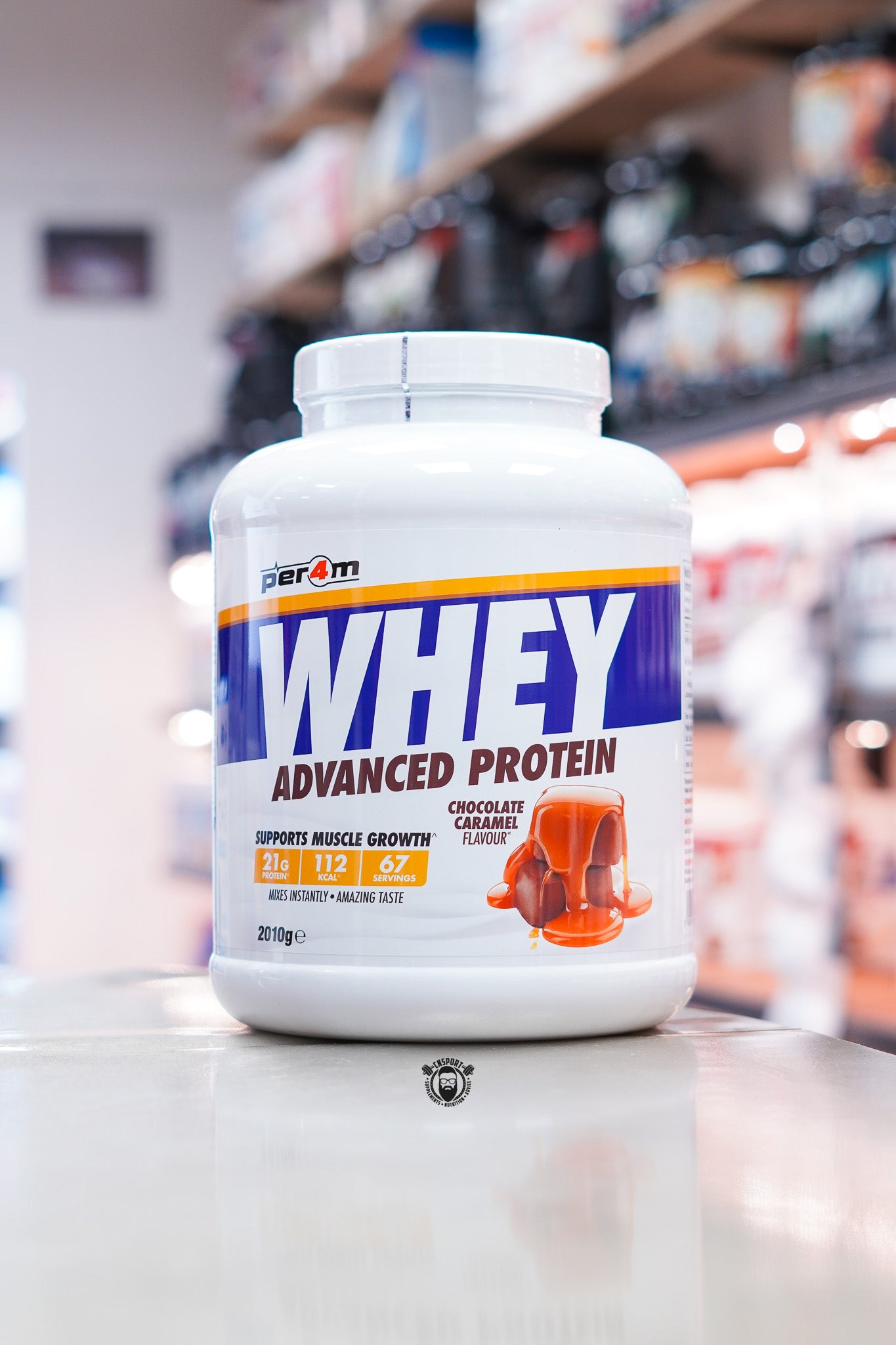 Per4m Whey Advanced Protein 2kg – Chocolate Caramel (Front)
Per4m Whey Advanced Protein in Chocolate Caramel flavour, 2.01kg tub providing 67 servings, displayed on a countertop in a supplement store. Front label highlights 21g protein, 112 calories per serving, and support for muscle growth.