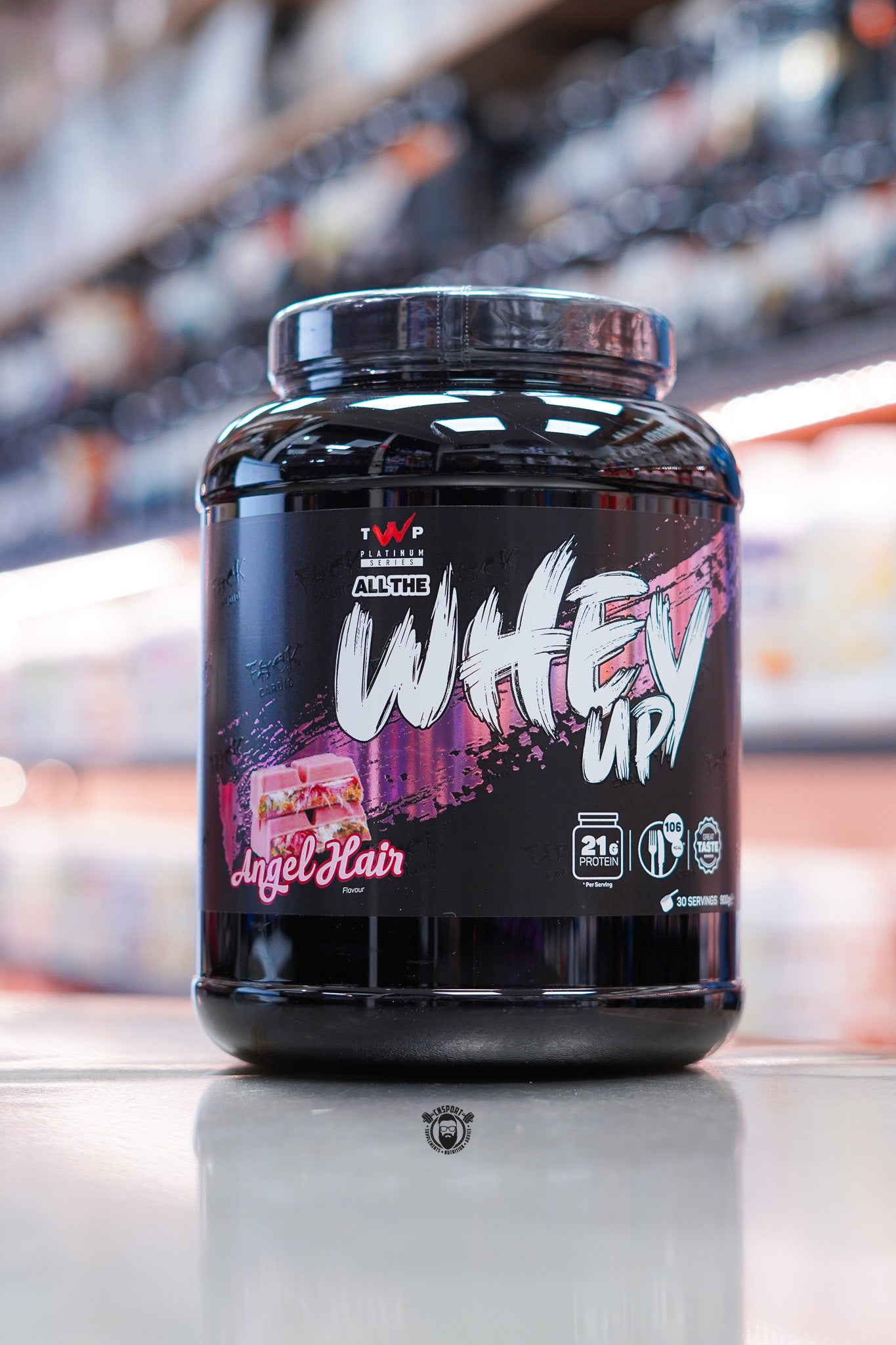 TWP Platinum Series All The Whey Up Angel Hair flavour 900g whey protein tub on retail counter with blurred supplement store background