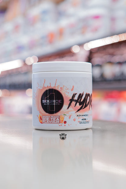 1 Source Supplements Hydrate advanced hydration powder tub in Sweet Peach Ice Tea flavour displayed on a retail counter with blurred supplement shelves behind.