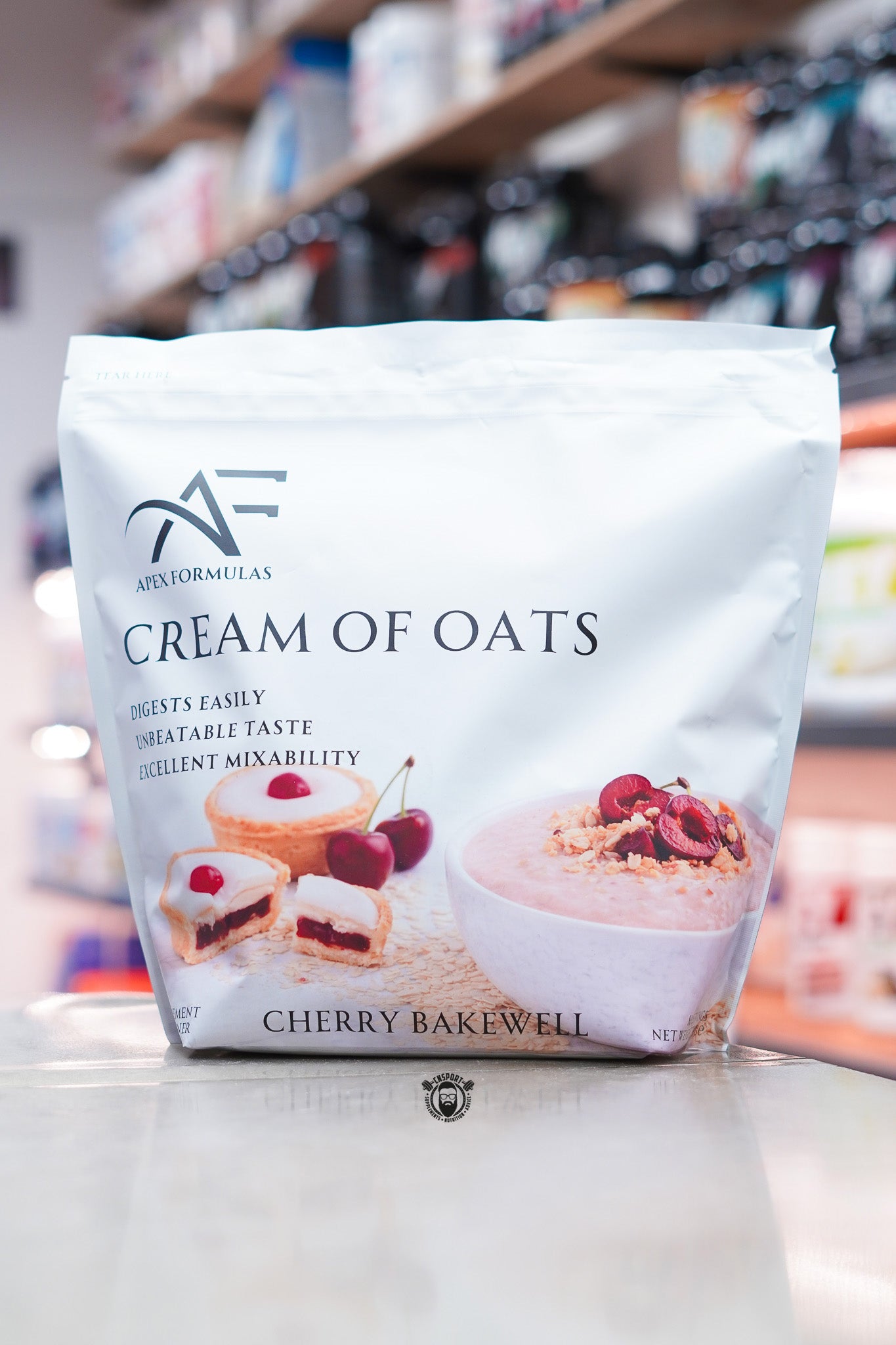 Apex Formulas Cream of Oats Cherry Bakewell flavour pouch displayed on a supplement store counter.