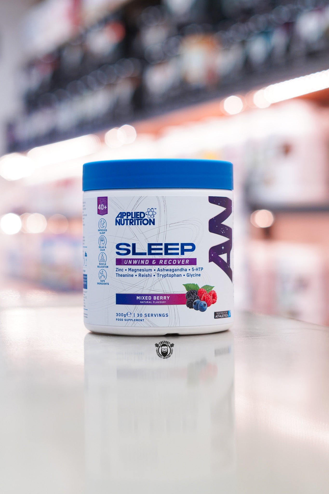 Applied Nutrition Sleep Unwind & Recover in Mixed Berry flavour, 300g tub with 30 servings, displayed on a countertop in a supplement store.