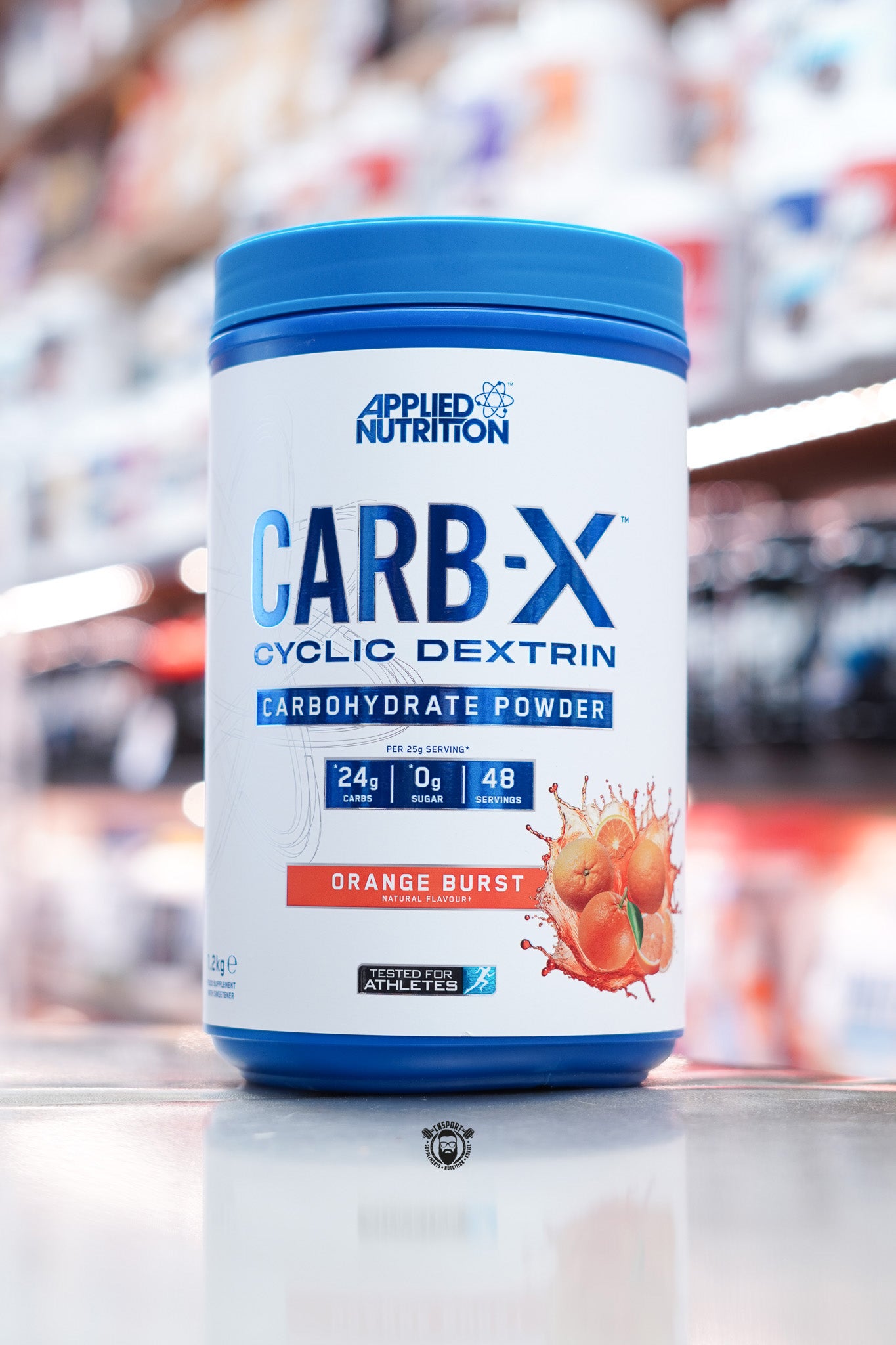 Front-facing image of Applied Nutrition Carb-X Orange Burst flavour with bold orange splash graphics and carbohydrate details per serving.