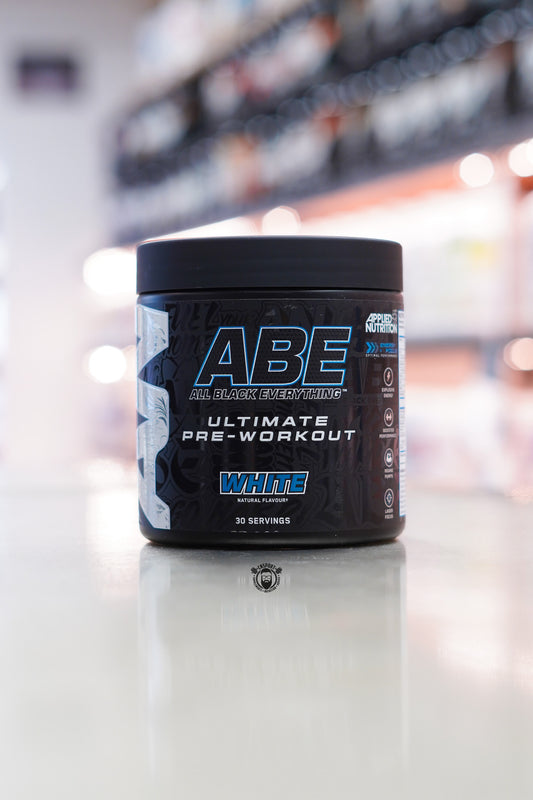Front view of Applied Nutrition ABE Ultimate Pre-Workout in White flavour, 30 servings, in a black tub displayed on a supplement store counter with a blurred retail background.