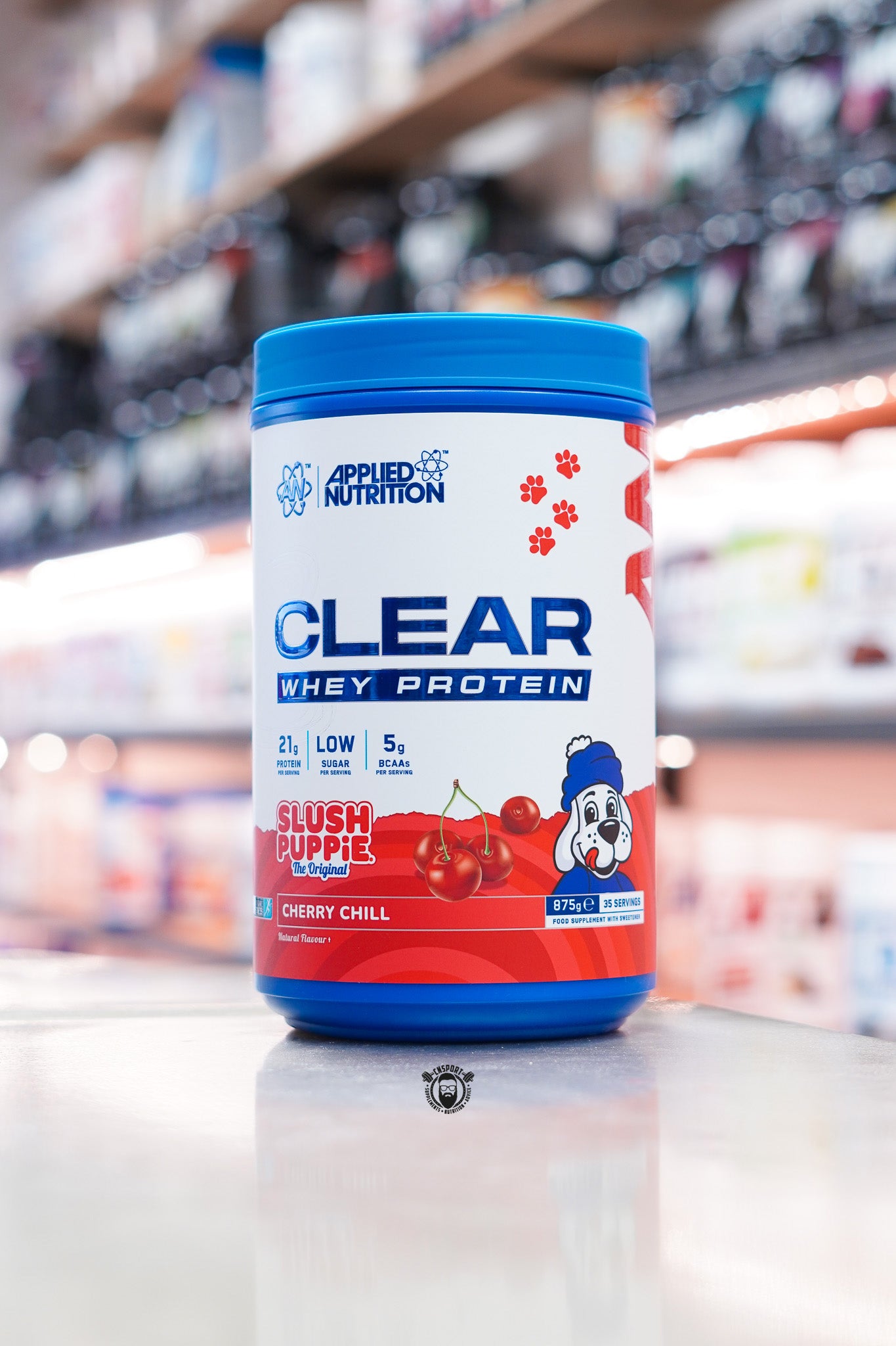 Applied Nutrition Clear Whey Protein Slush Puppie Cherry Chill flavour 875g tub displayed on a supplement shop counter.