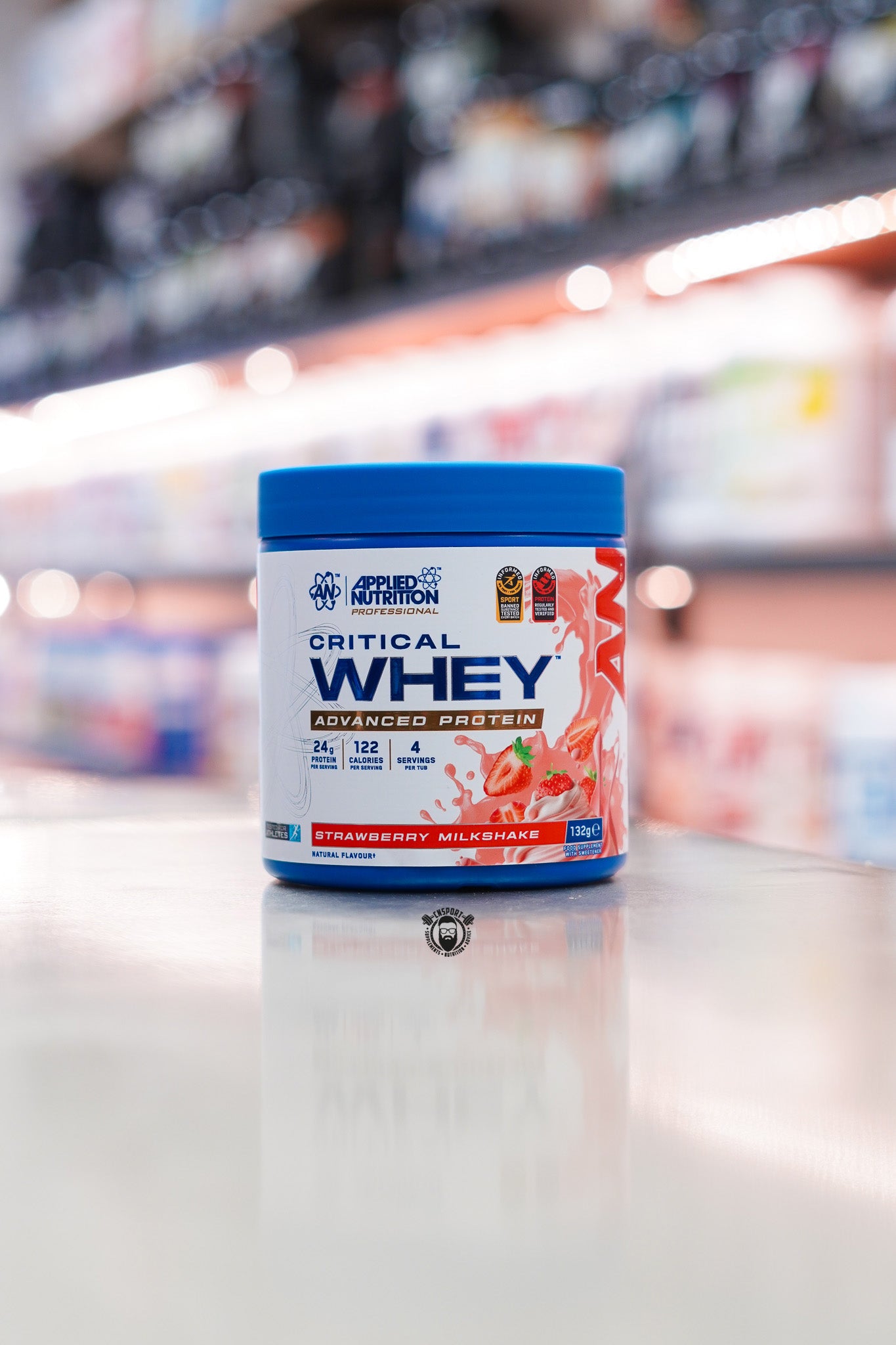 Applied Nutrition Critical Whey 132g protein powder sample tub, Strawberry Milkshake flavour, displayed on a supplement store counter.