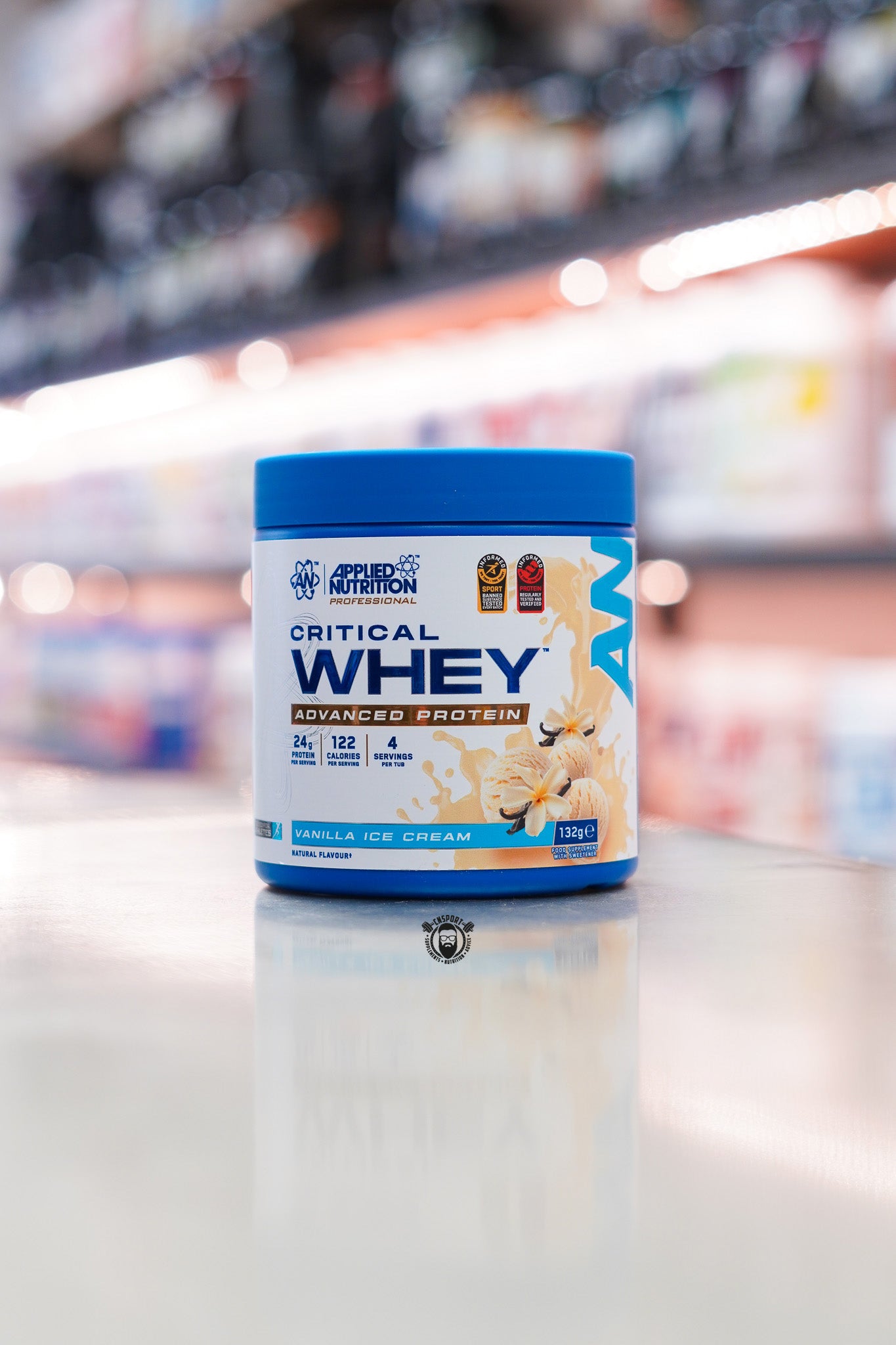 Applied Nutrition Critical Whey 132g protein powder sample tub, Vanilla Ice Cream flavour, displayed on a supplement store counter.