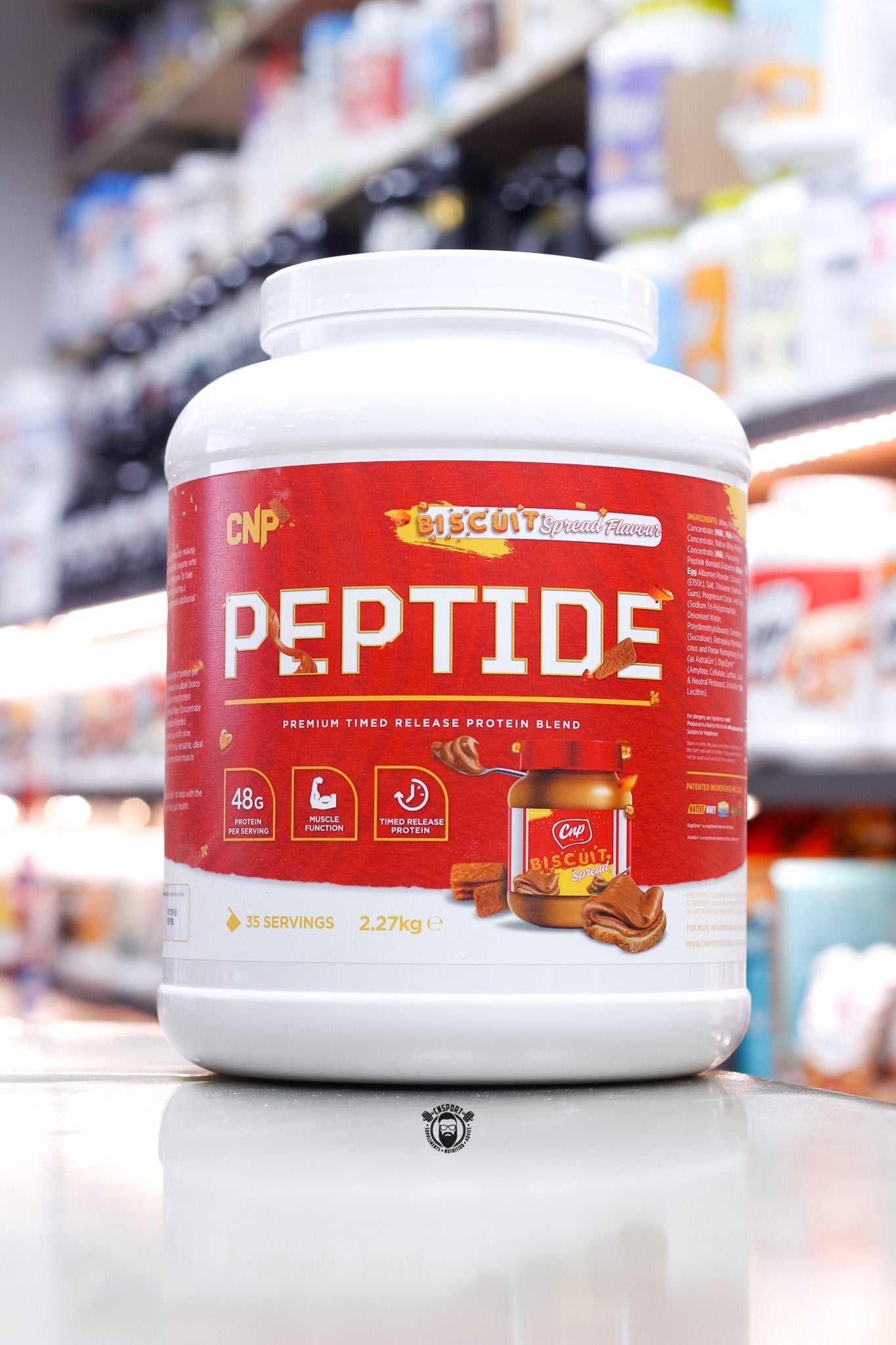 2.27kg tub of CNP Peptide timed release protein blend in Biscuit Spread Flavour, with a bold red label, biscuit spread jar imagery, and nutritional highlights including 48g protein per serving and 35 servings total.