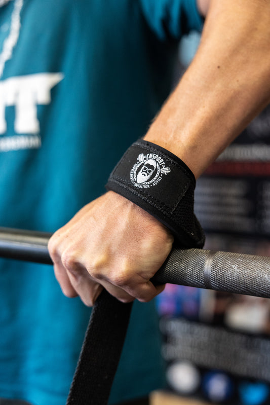 A close-up of a hand gripping a knurled barbell using a black CNSport cotton lifting strap with the CNSport logo visible on the wrist.