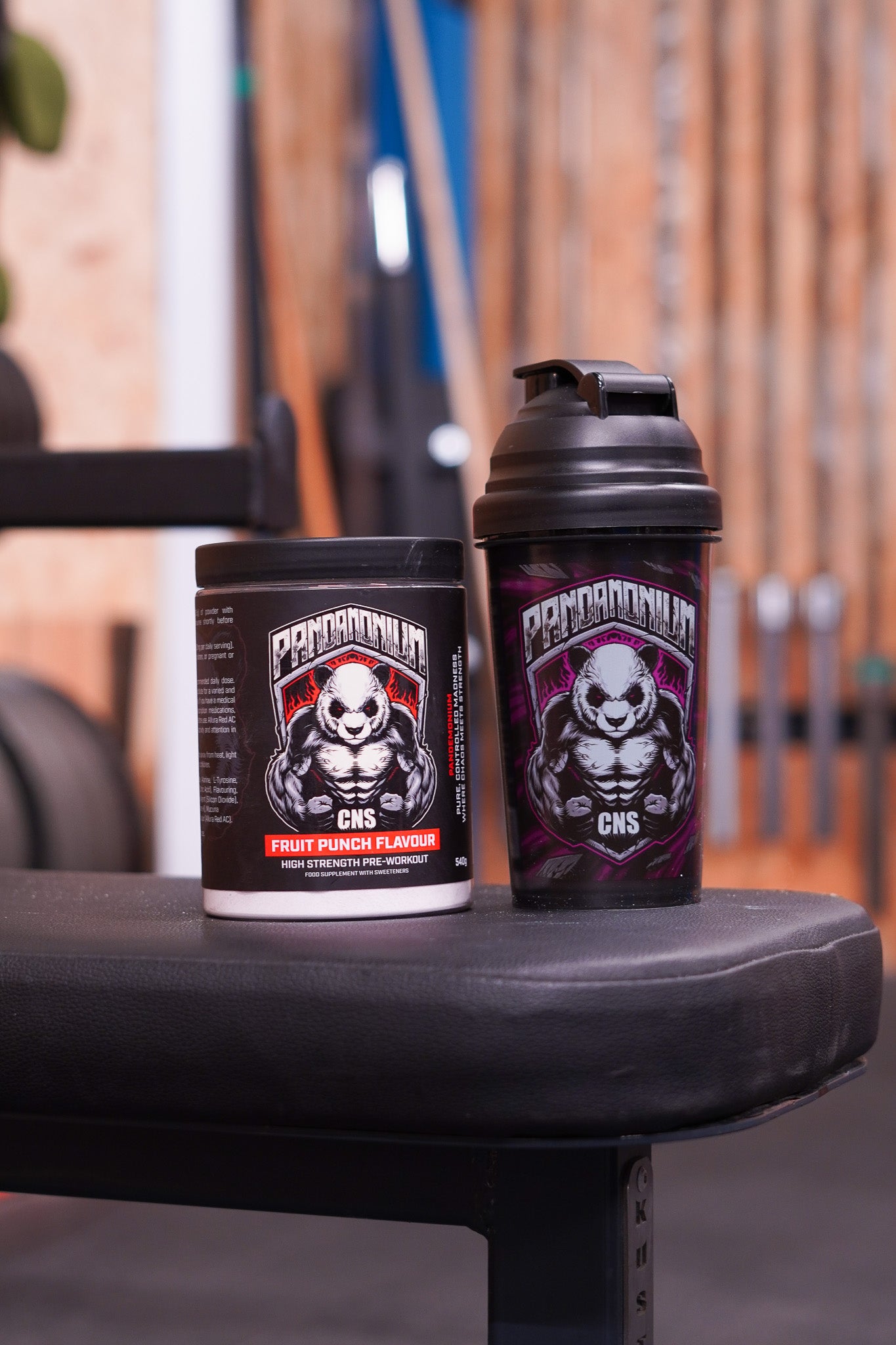 CNSport Pandamonium Fruit Punch Pre-Workout tub displayed on a gym bench alongside a black Pandamonium shaker featuring the aggressive panda logo.