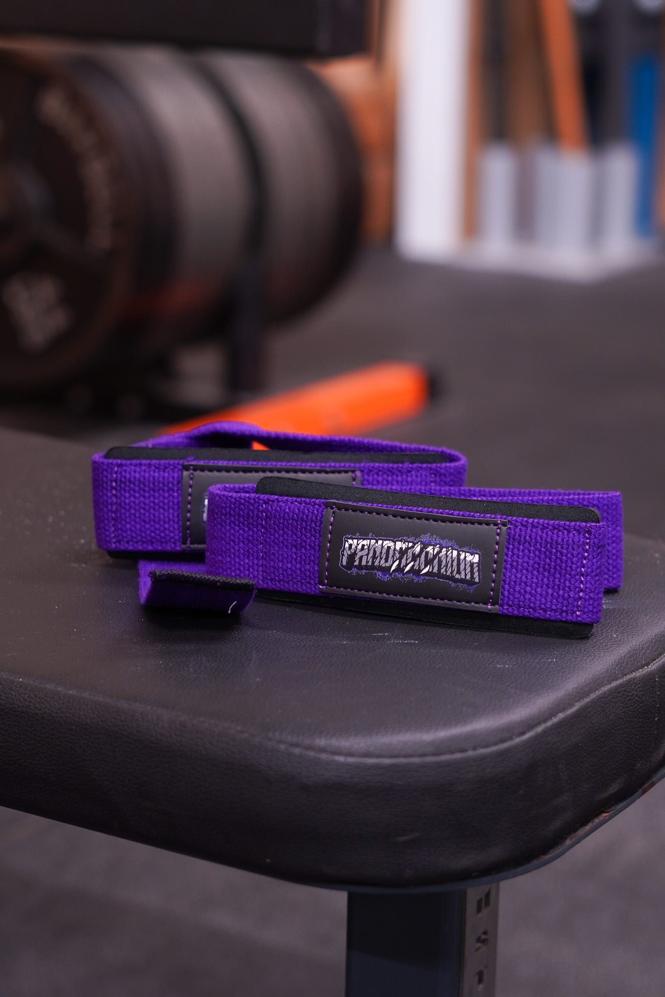 Close-up of purple Pandamonium lifting straps on a gym bench highlighting the stitched logo.
