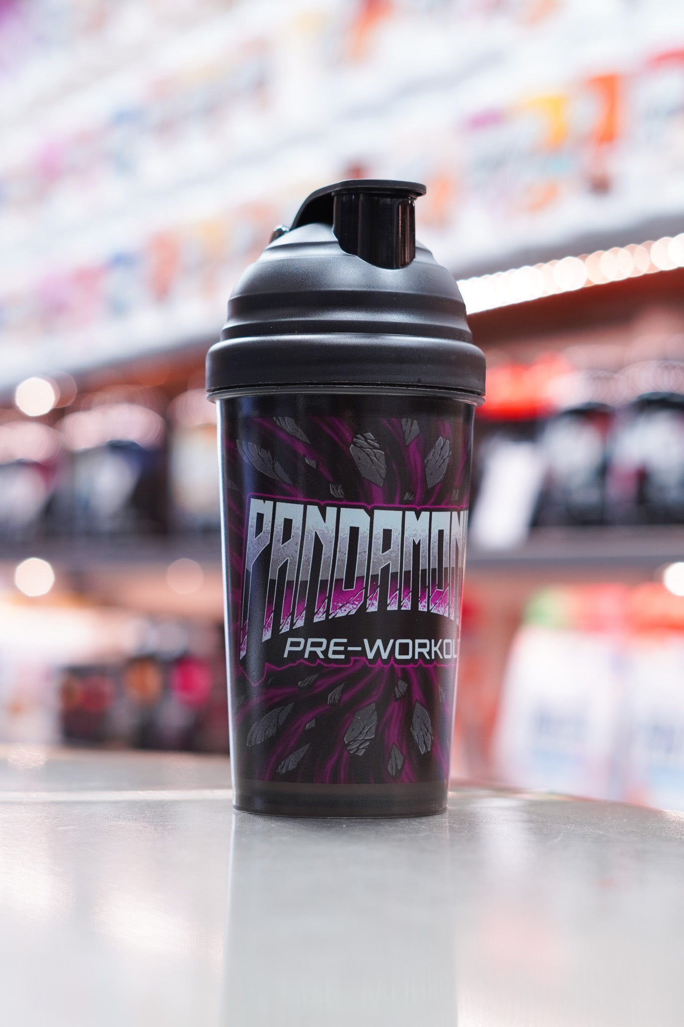 Front-facing view of the CNSport Pandamonium shaker displaying the large metallic “PANDAMONIUM PRE-WORKOUT” logo over a purple cracked-stone pattern, with soft store lighting in the background.