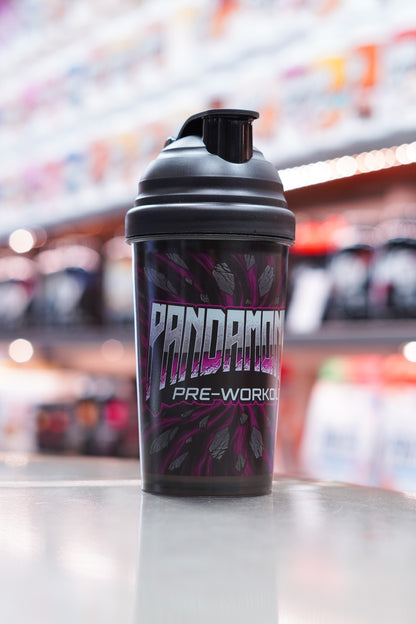 Front-facing view of the CNSport Pandamonium shaker displaying the large metallic “PANDAMONIUM PRE-WORKOUT” logo over a purple cracked-stone pattern, with soft store lighting in the background.