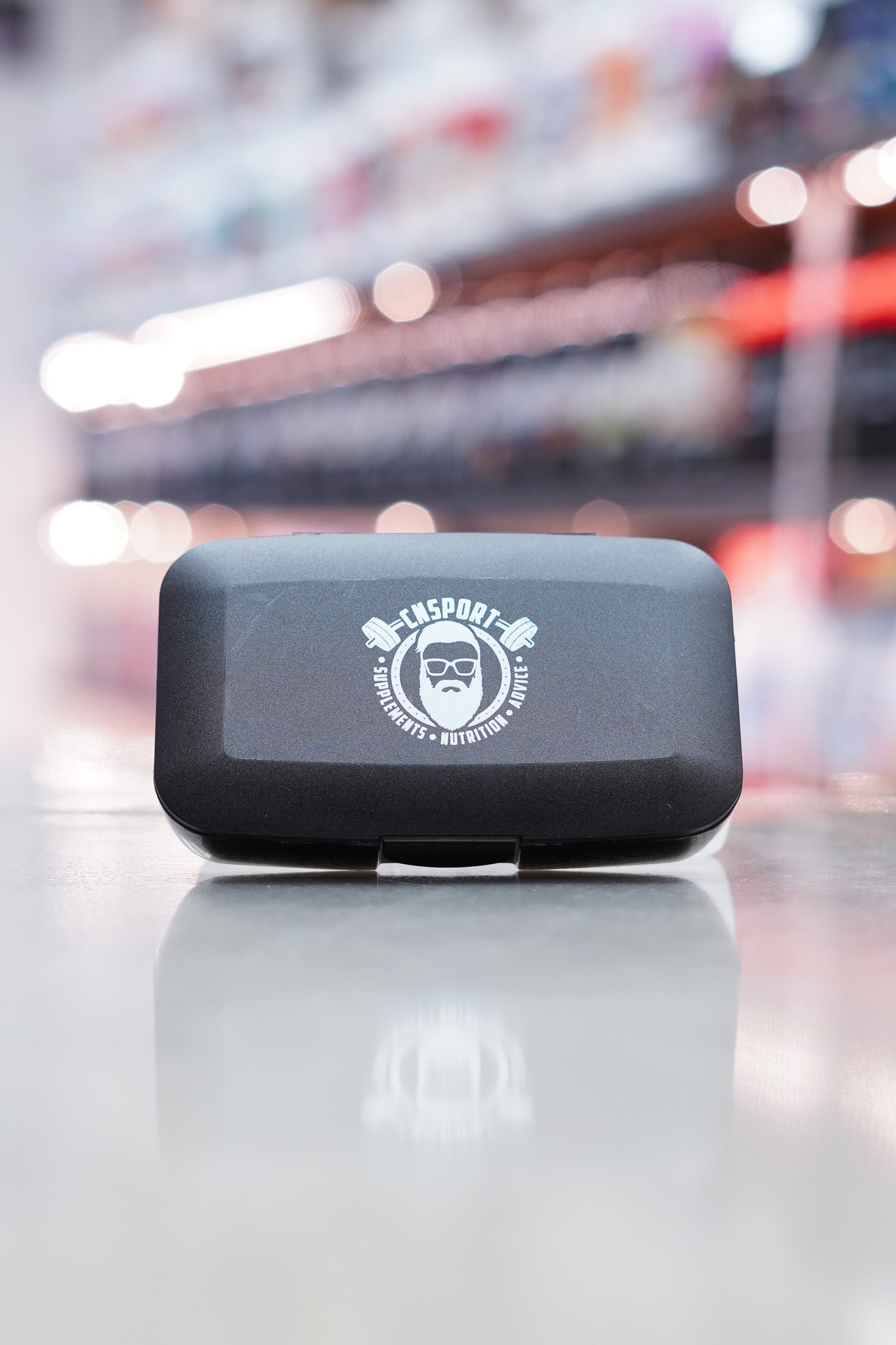 Closed CNSport clear pill box with black CNSport logo displayed on the front lid, positioned on a glossy countertop.