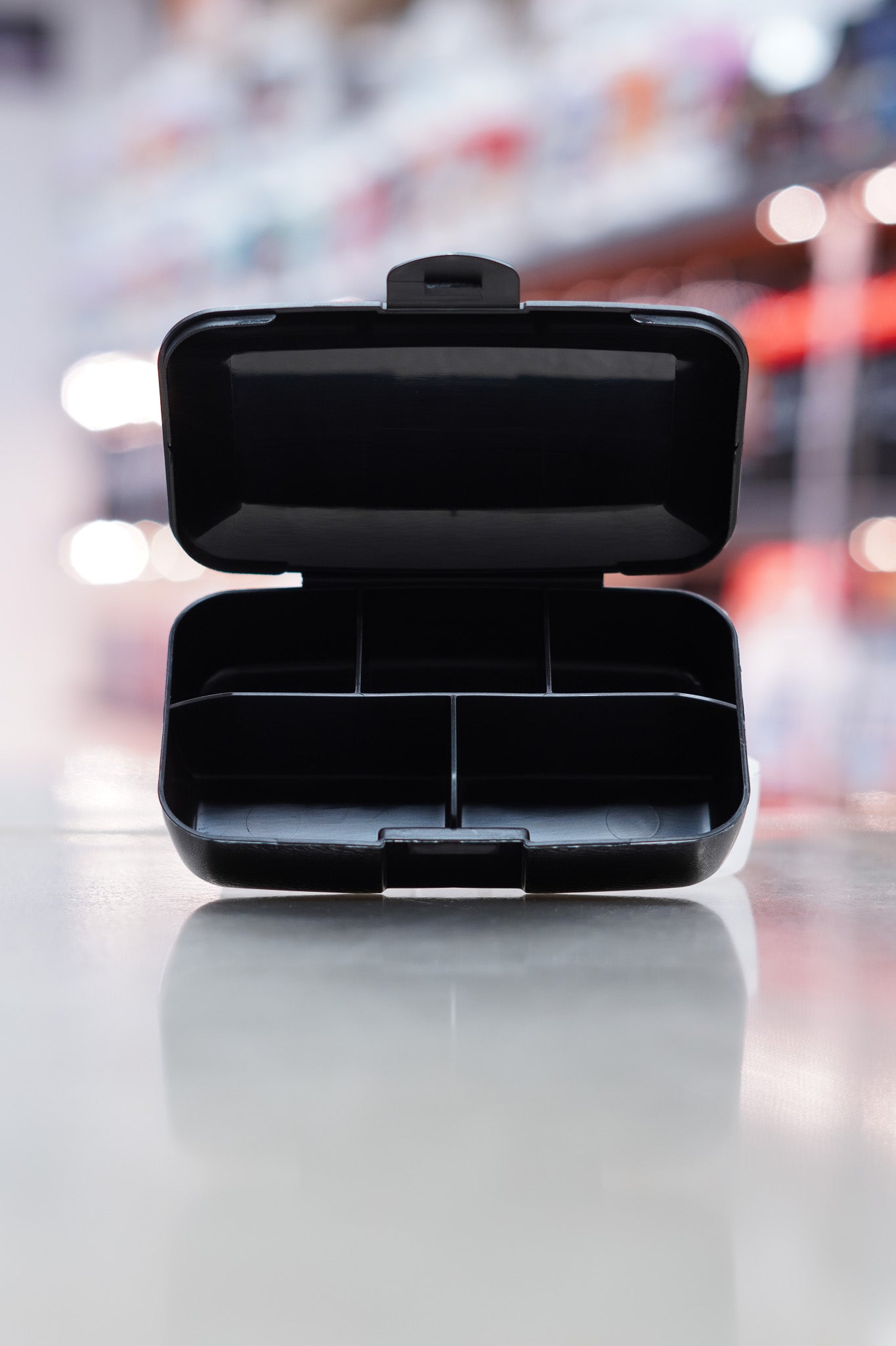 Open CNSport black pill box showing five internal compartments for supplement or capsule storage, photographed on a reflective counter surface.