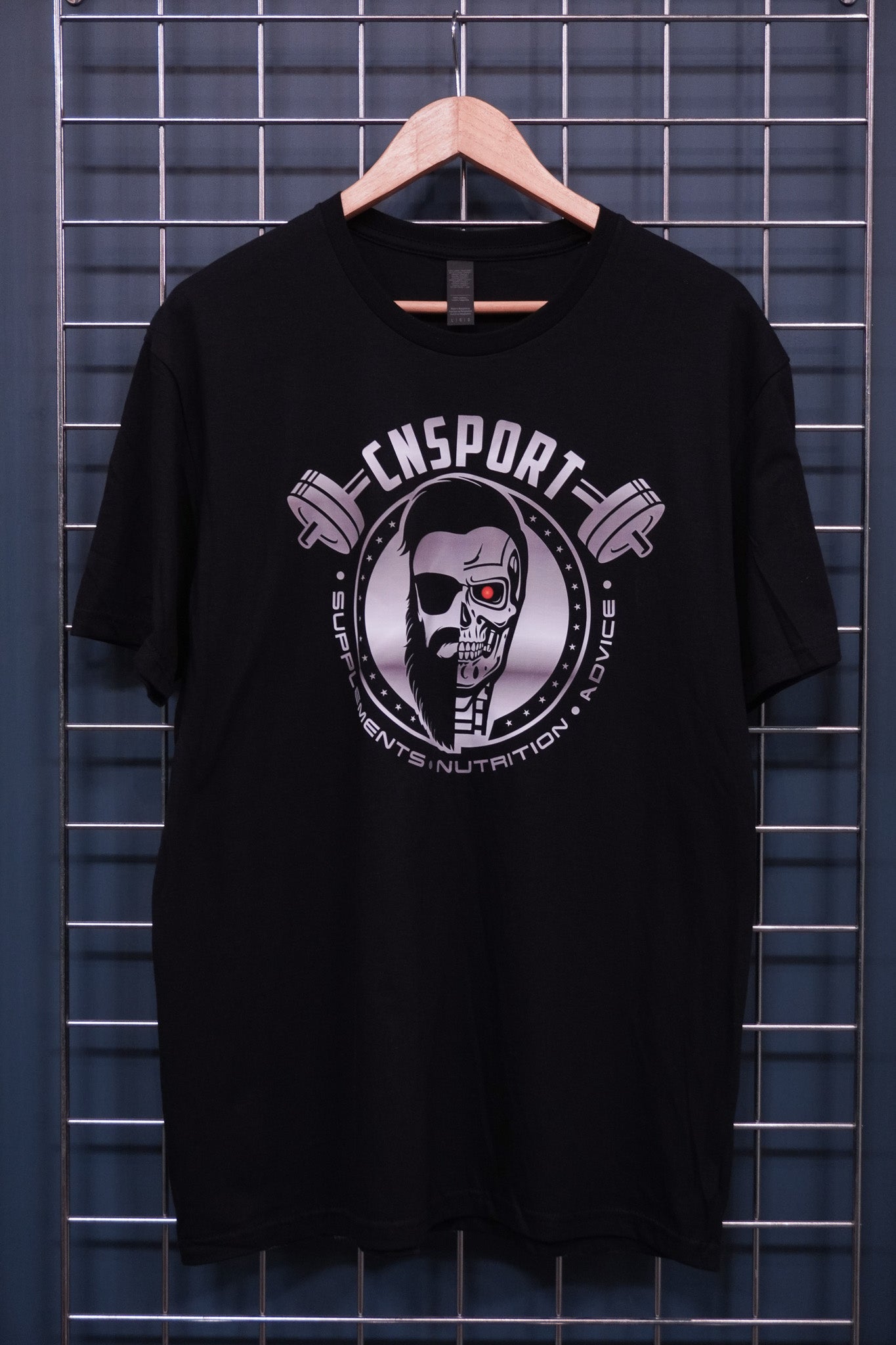Black CNSport Terminator graphic T-shirt hanging on display wall featuring skull and machine hybrid logo with barbell design