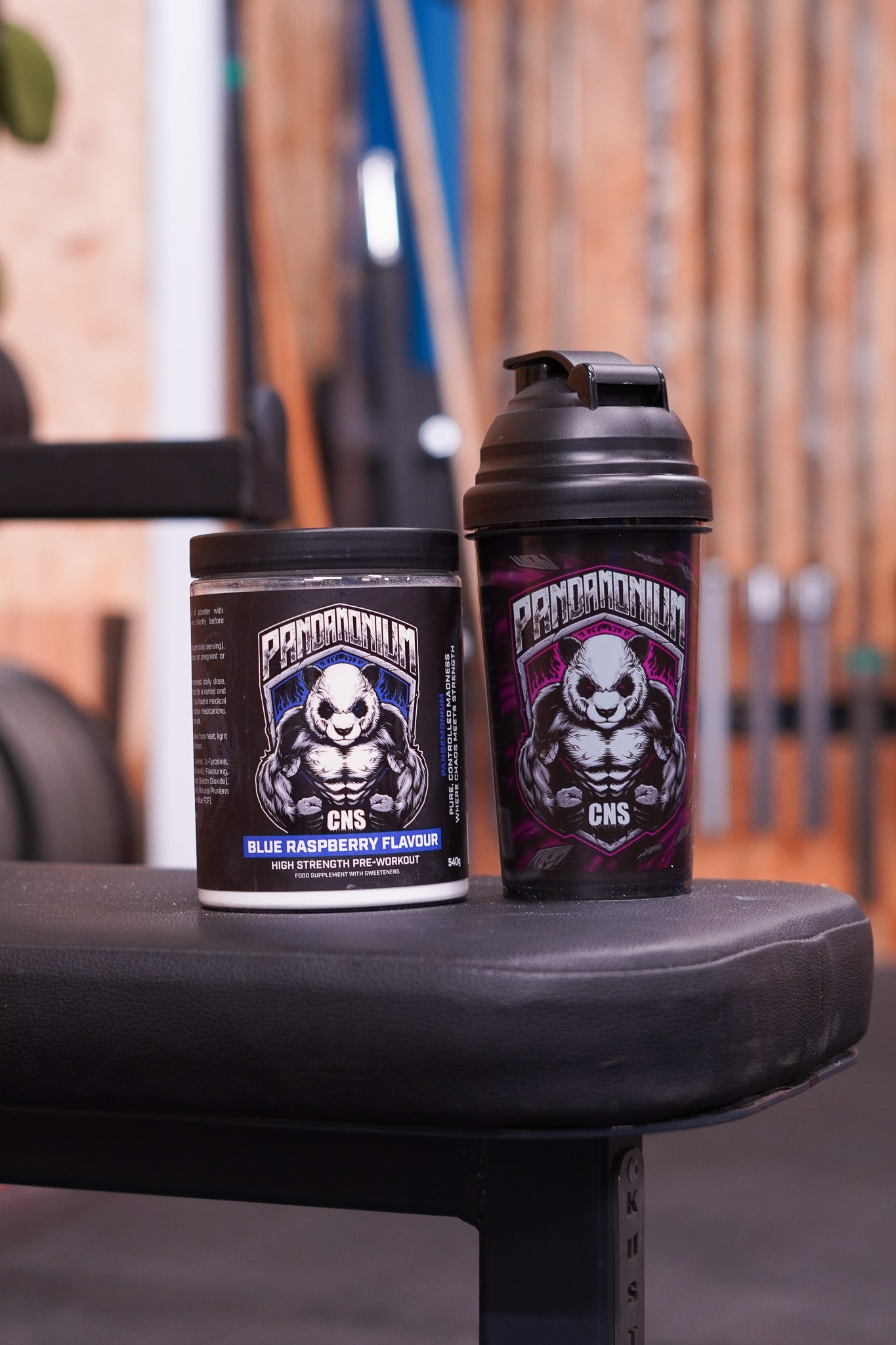 CNSport Pandamonium Blue Raspberry Pre-Workout tub displayed on a gym bench next to a black Pandamonium shaker with the muscular panda logo.