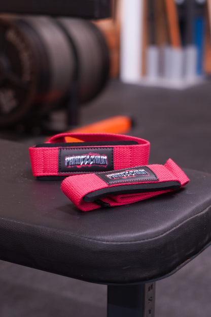 Pink Pandamonium lifting straps displayed on a gym bench with gym equipment blurred behind.