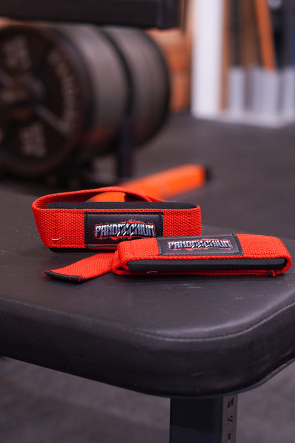 Red Pandamonium lifting straps resting on a gym bench with a blurred gym setup behind them.