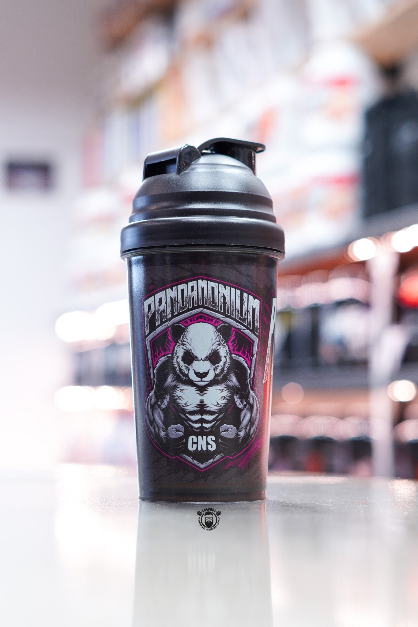 CNSport Pandamonium 600ml black shaker bottle with flip lid, featuring muscular panda logo in purple and white, displayed on counter in supplement store.