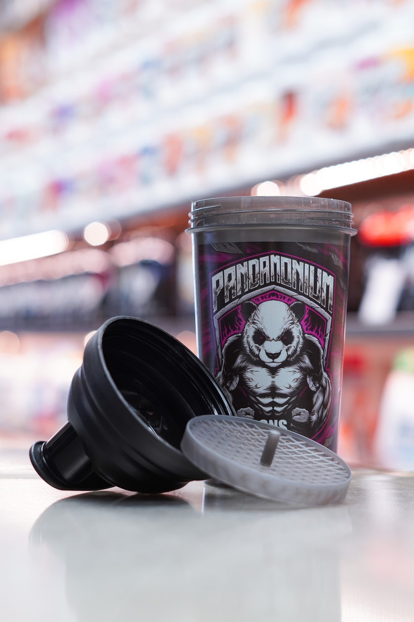 CNSport Pandamonium shaker shown opened and disassembled, with the lid and mixing grid placed in the foreground and the main shaker body standing behind displaying the panda mascot graphic.