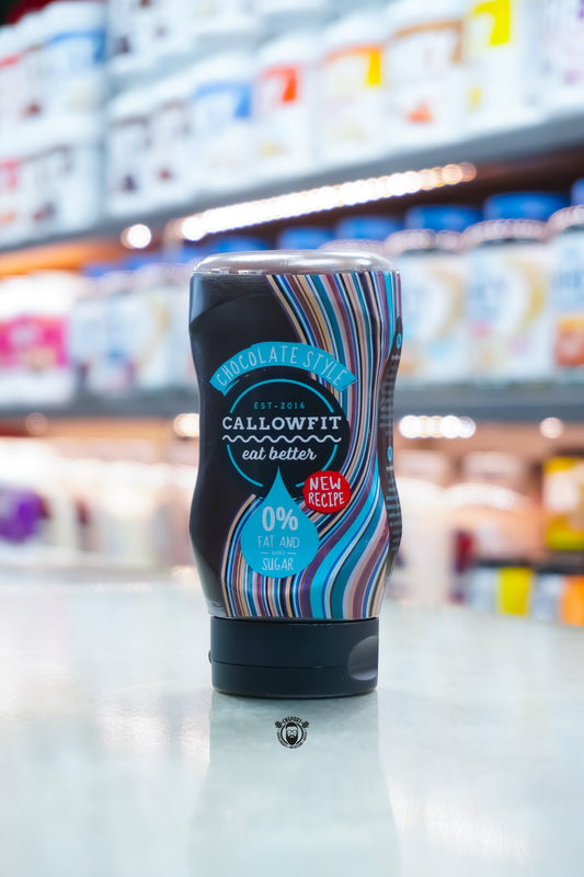 Callowfit Chocolate Style Sauce 300ml bottle with new recipe packaging, sugar-free, 0% fat, displayed upright on a countertop with a blurred supplement store background.
