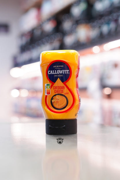 Callowfit Cheddar Cheese Style low sugar sauce bottle with Nutri-Score B, displayed upright on a countertop in a supplement store.