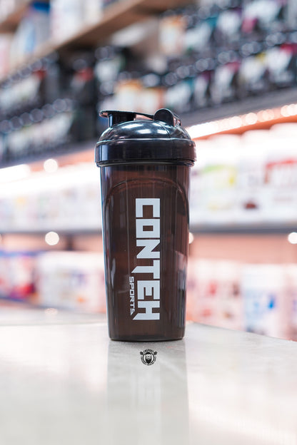 Smoky black Conteh Sports 700ml ball shaker bottle with black flip-top lid displayed on a supplement shop counter.
