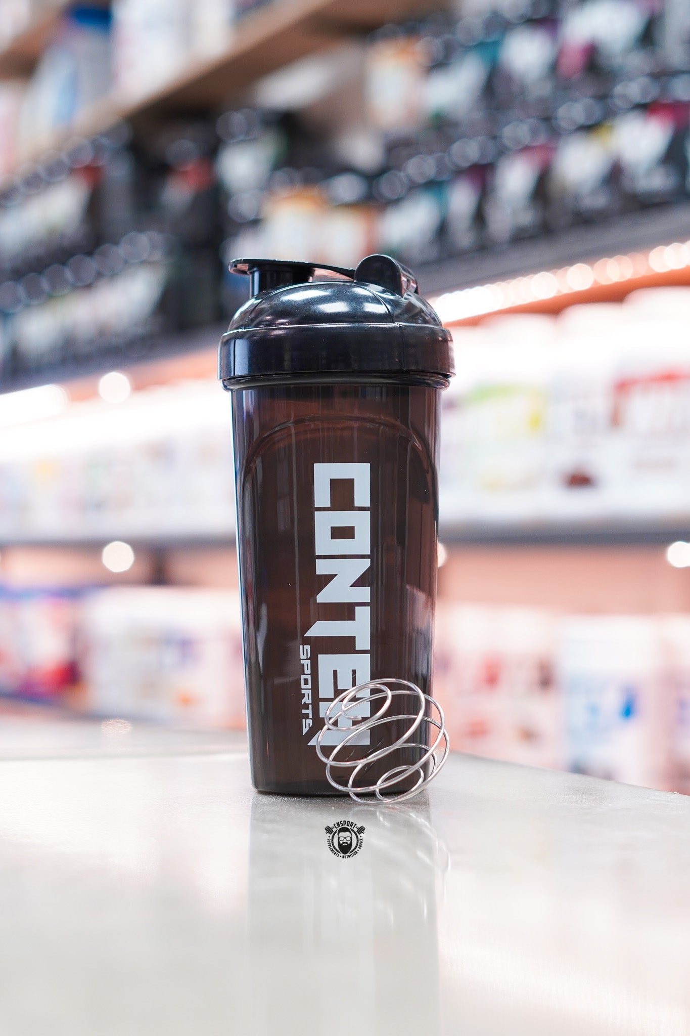 Smoky black Conteh Sports 700ml ball shaker bottle displayed with a stainless steel mixing ball on a supplement shop counter.