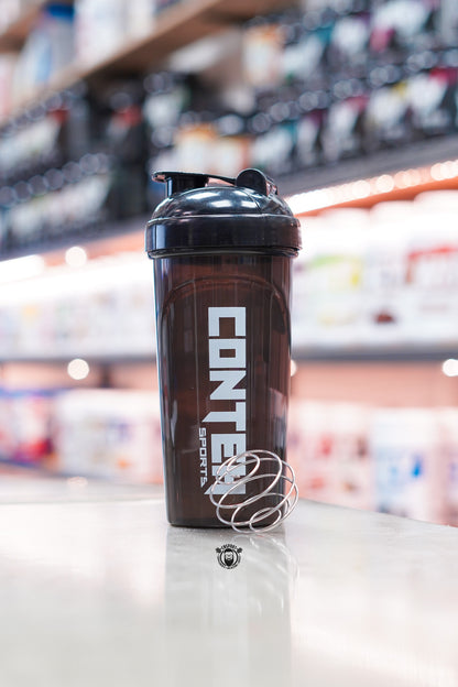 Smoky black Conteh Sports 700ml ball shaker bottle displayed with a stainless steel mixing ball on a supplement shop counter.