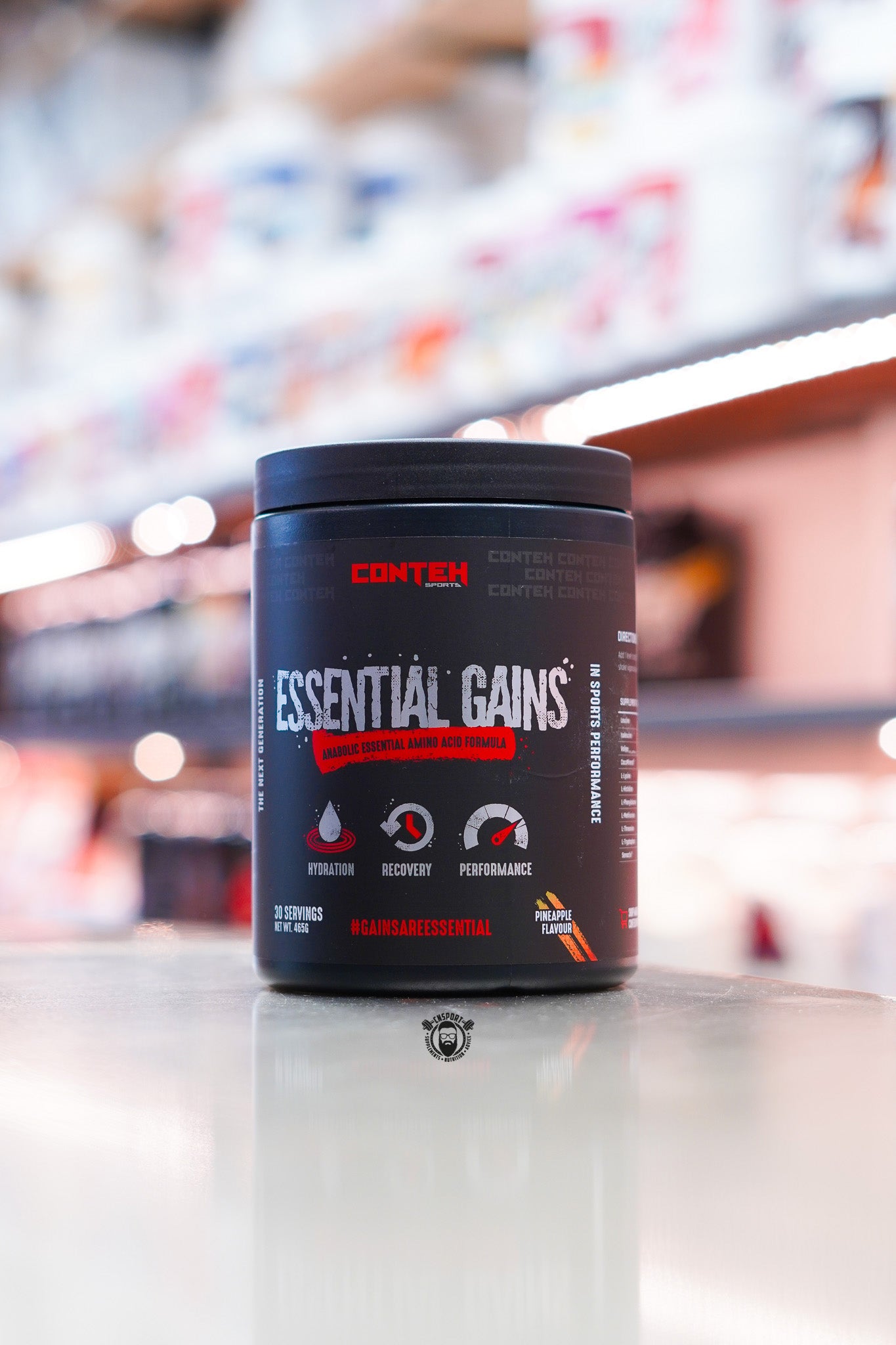 Conteh Sports Essential Gains amino acid formula tub, Pineapple flavour, displayed on supplement store counter.