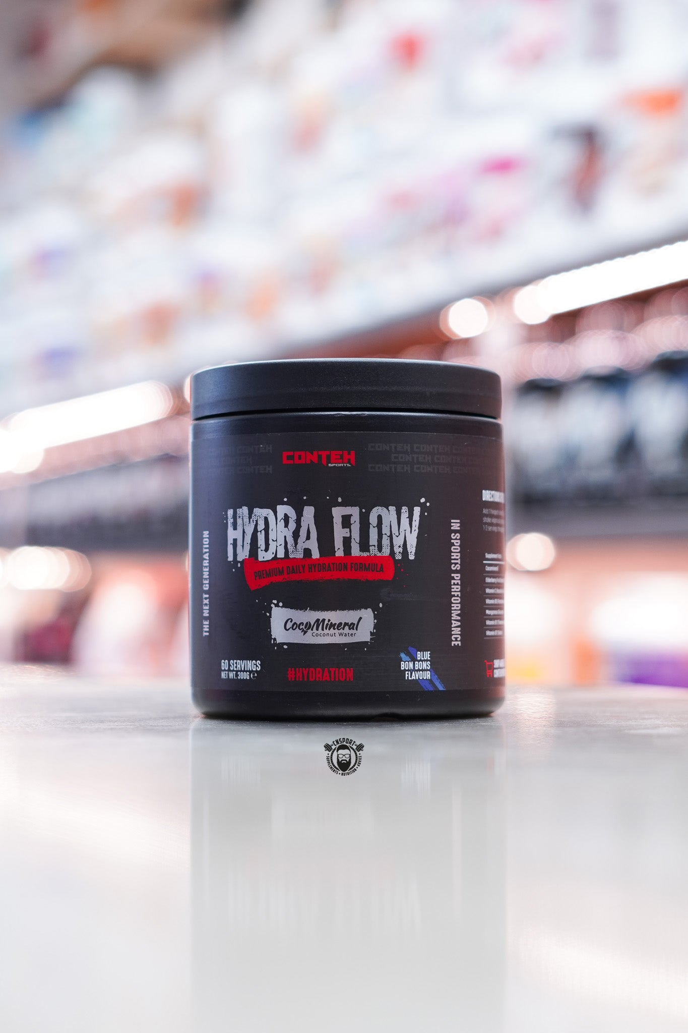 Conteh Sports Hydra Flow hydration powder in Blue Bon Bons flavour – 60 serving tub featuring CocoMineral, placed in retail store environment.