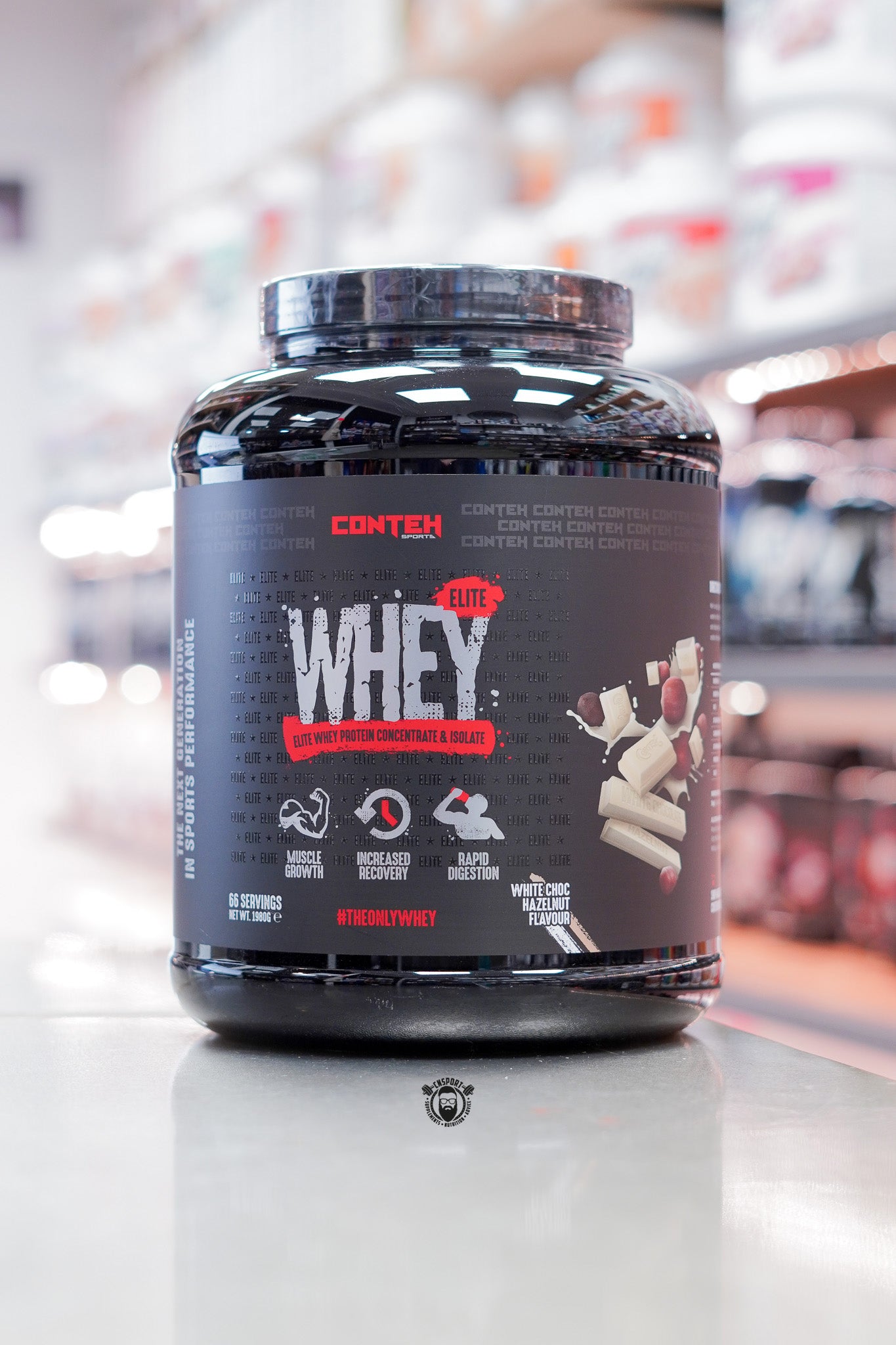 Conteh Sports Whey Elite protein powder, White Chocolate Hazelnut flavour, 66 servings (1.98kg) black tub displayed on supplement store counter.
