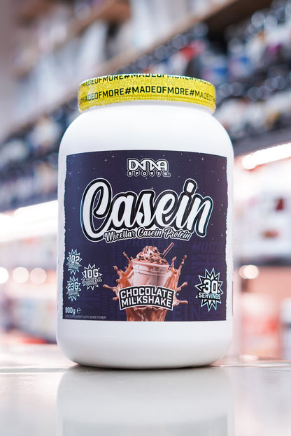 DNA Sports Casein Micellar Casein Protein Chocolate Milkshake 900g 30 servings tub on retail counter with blurred supplement store background