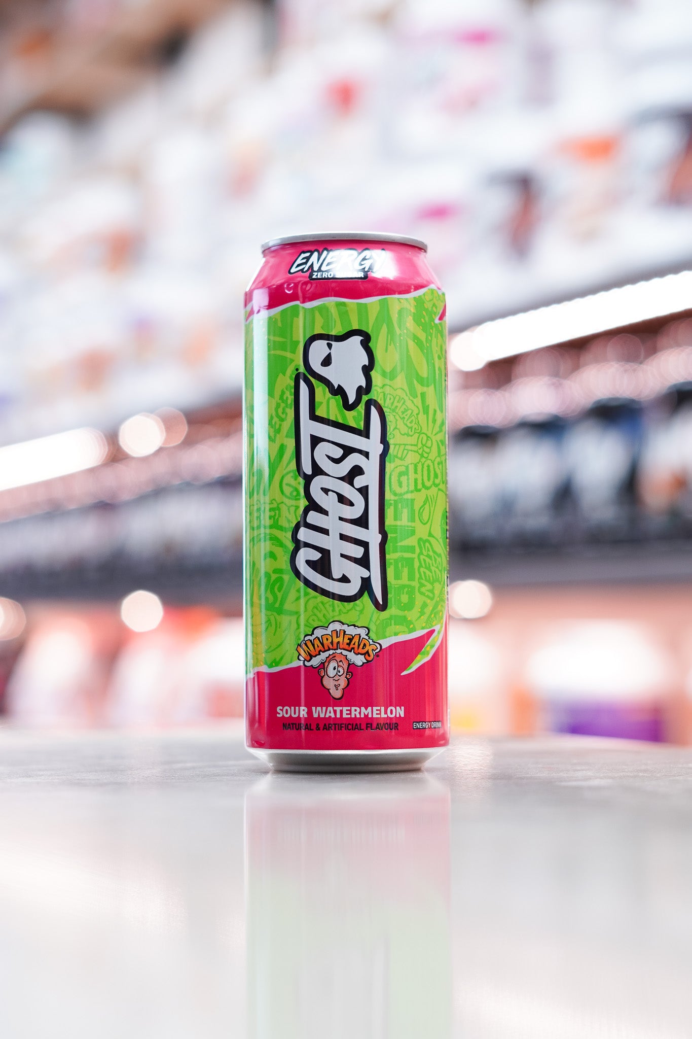 Bright green and pink Warheads-themed Ghost Energy Drink in Sour Watermelon flavor, featuring cartoon artwork and ghost branding, photographed on a store counter.