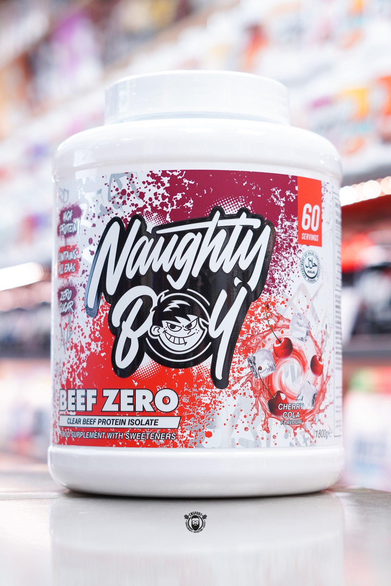 A large white tub of Naughty Boy Beef Zero clear beef protein isolate in Cherry Cola flavour, with a red splatter design and images of cherries and ice cubes on the label