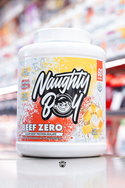 Front of Naughty Boy Beef Zero Iced Mango 1.8kg tub with yellow and orange splatter design, Naughty Boy logo, and diced mango imagery.