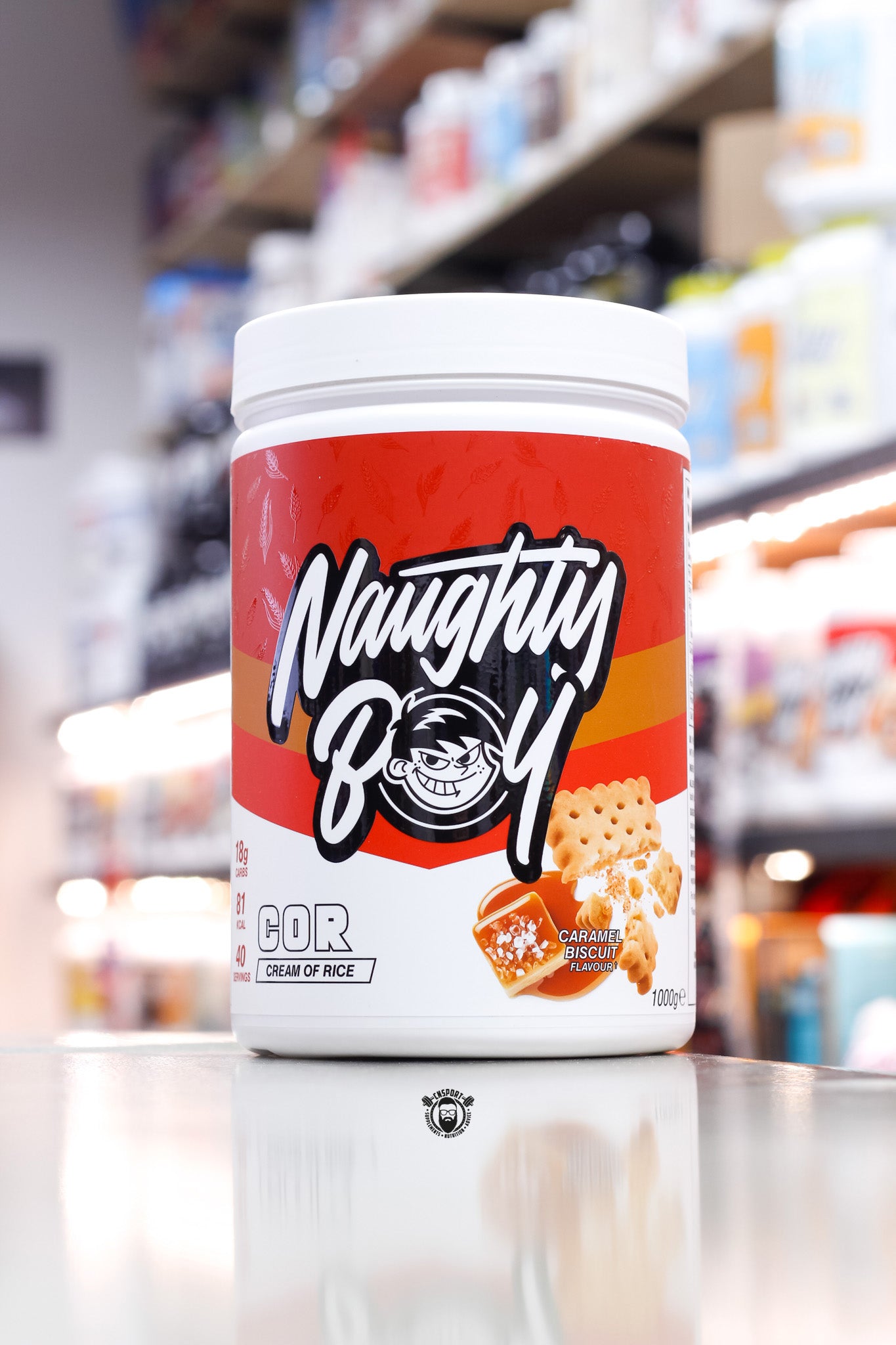 1kg Naughty Boy COR Cream of Rice in Caramel Biscuit flavour, with a rich red and caramel-toned label showcasing biscuit and caramel graphics.
