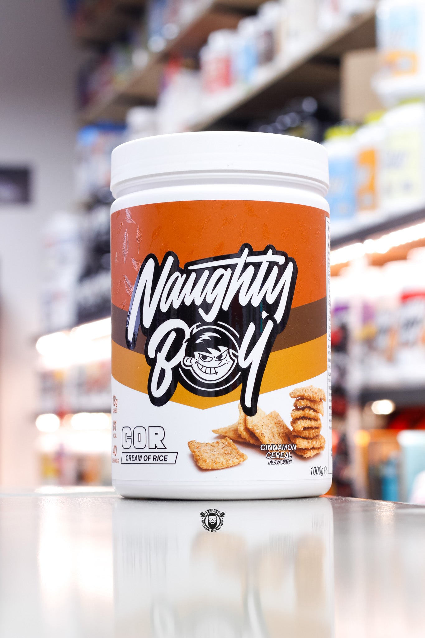 1kg tub of Naughty Boy COR Cream of Rice in Cinnamon Cereal flavour, with an orange-brown label and graphics of crunchy cinnamon cereal pieces.