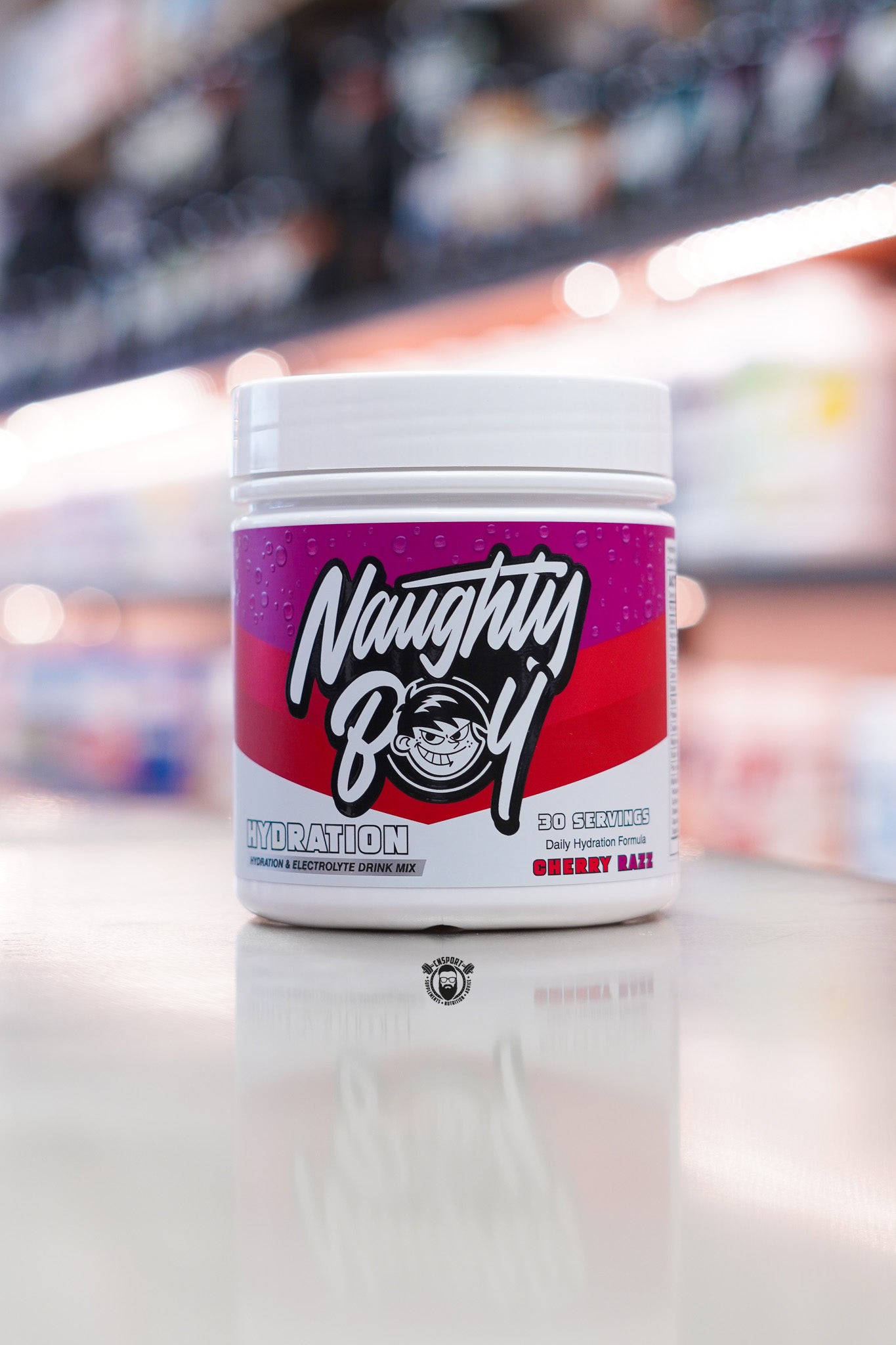 Naughty Boy Hydration Cherry Razz electrolyte drink mix tub displayed on a supplement store counter.