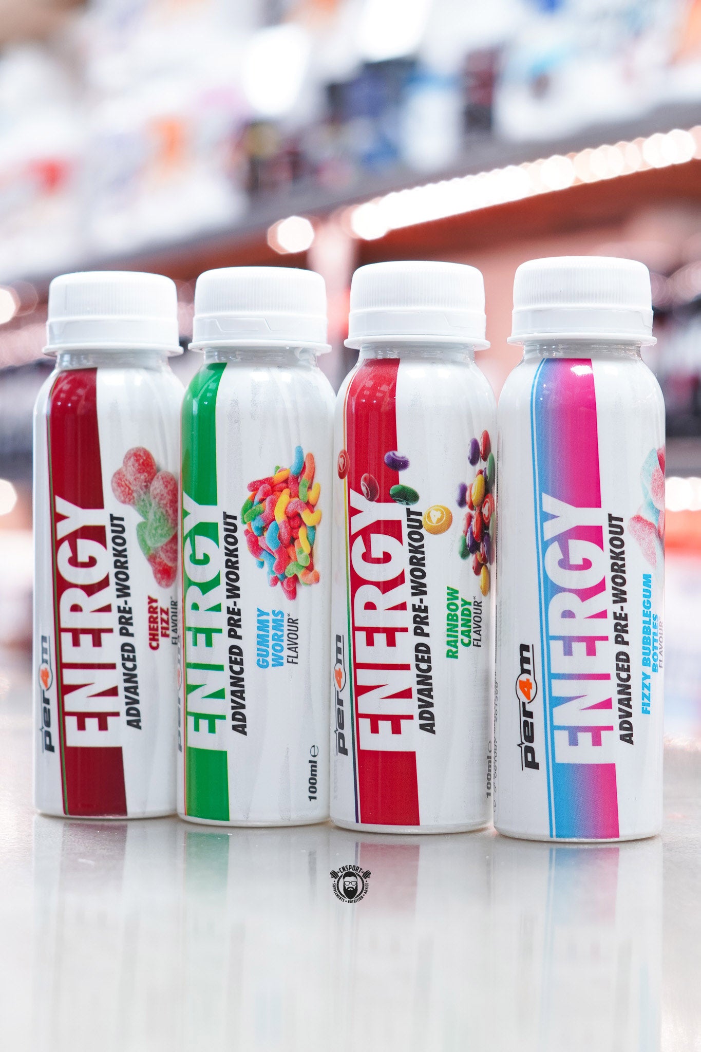Group shot of all four Per4m Energy Pre-Workout Shot flavours  Cherry Fizz, Gummy Worms, Rainbow Candy, and Fizzy Bubblegum Bottles arranged together on a reflective surface.