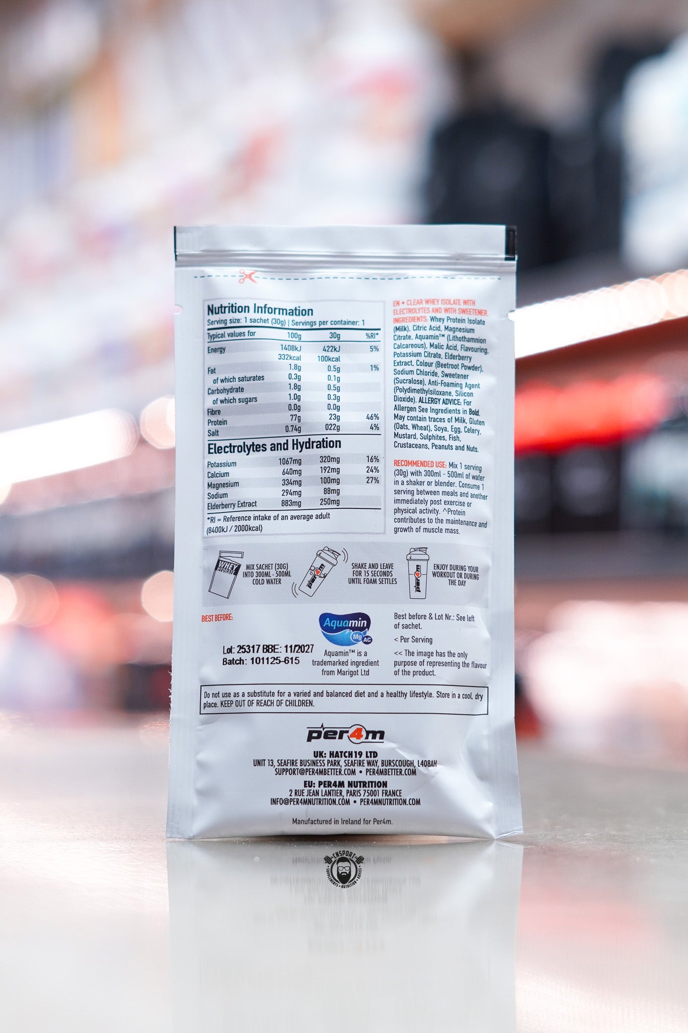 Per4m Whey Hydrate 30g sample sachet rear panel showing nutrition information and ingredients, displayed on counter in supplement store.