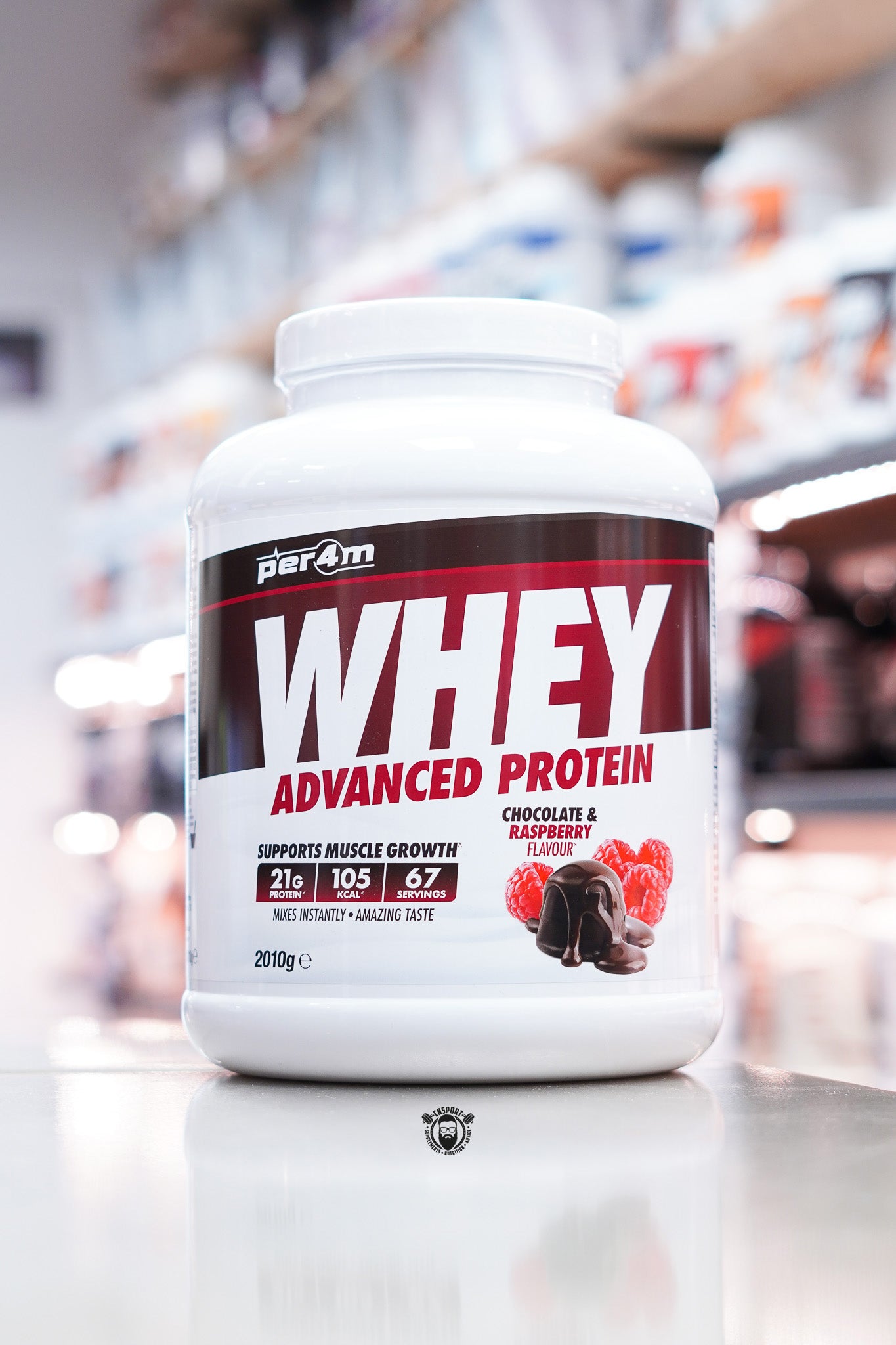 Per4m Whey Advanced Protein powder tub, Chocolate & Raspberry flavour, 2kg, displayed on supplement store counter.