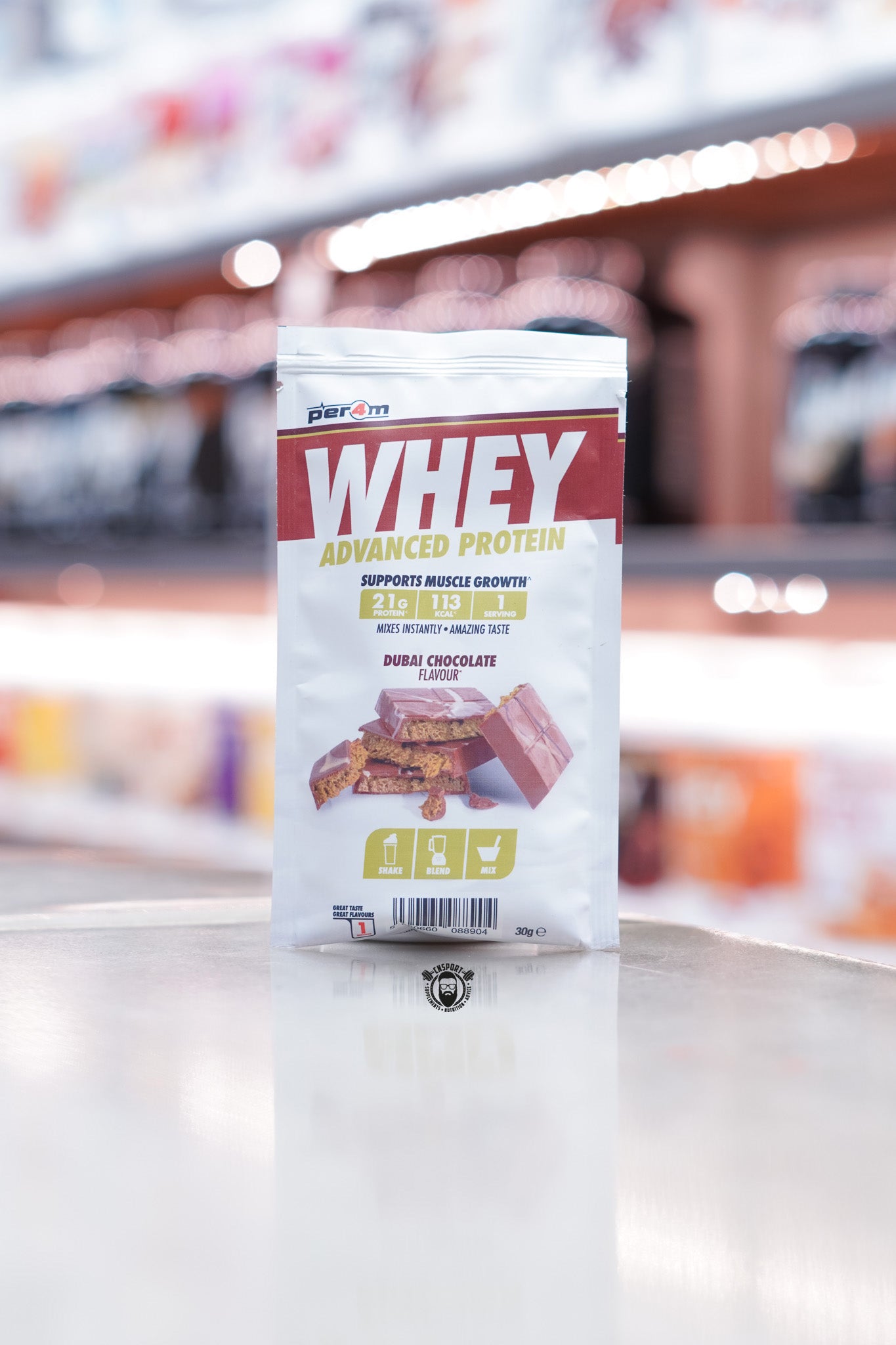 Front of a Per4m Whey Advanced Protein sample pouch in Dubai Chocolate flavour, showing 21g protein, 113 kcal, and 1 serving. Features image of chocolate pieces and gold shake/blend/mix icons.