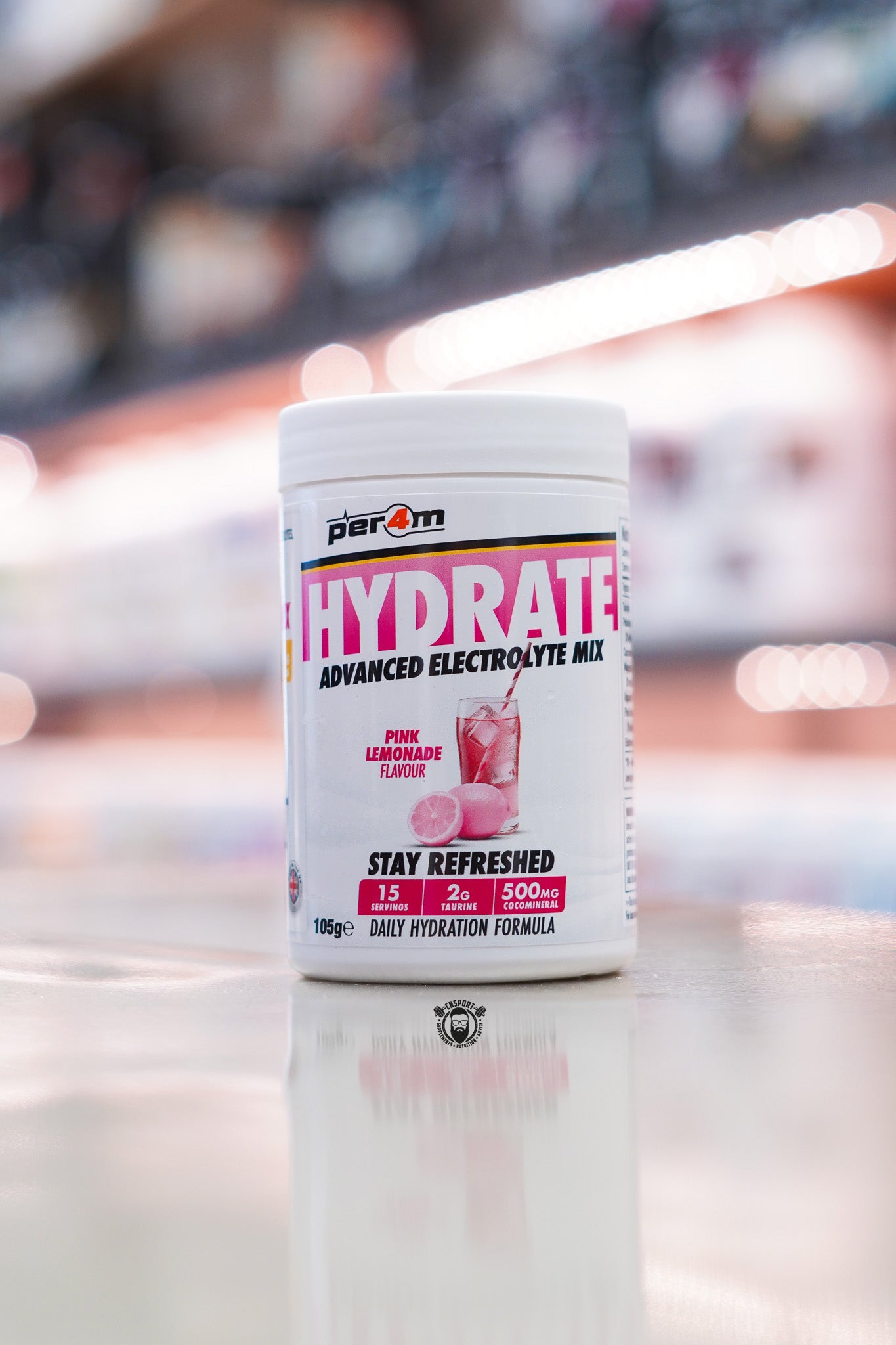 Per4m Hydrate Advanced Electrolyte Mix in Pink Lemonade flavour, featuring 2g taurine, CocoMineral®, 15 servings and a daily hydration formula, displayed on a supplement store counter.