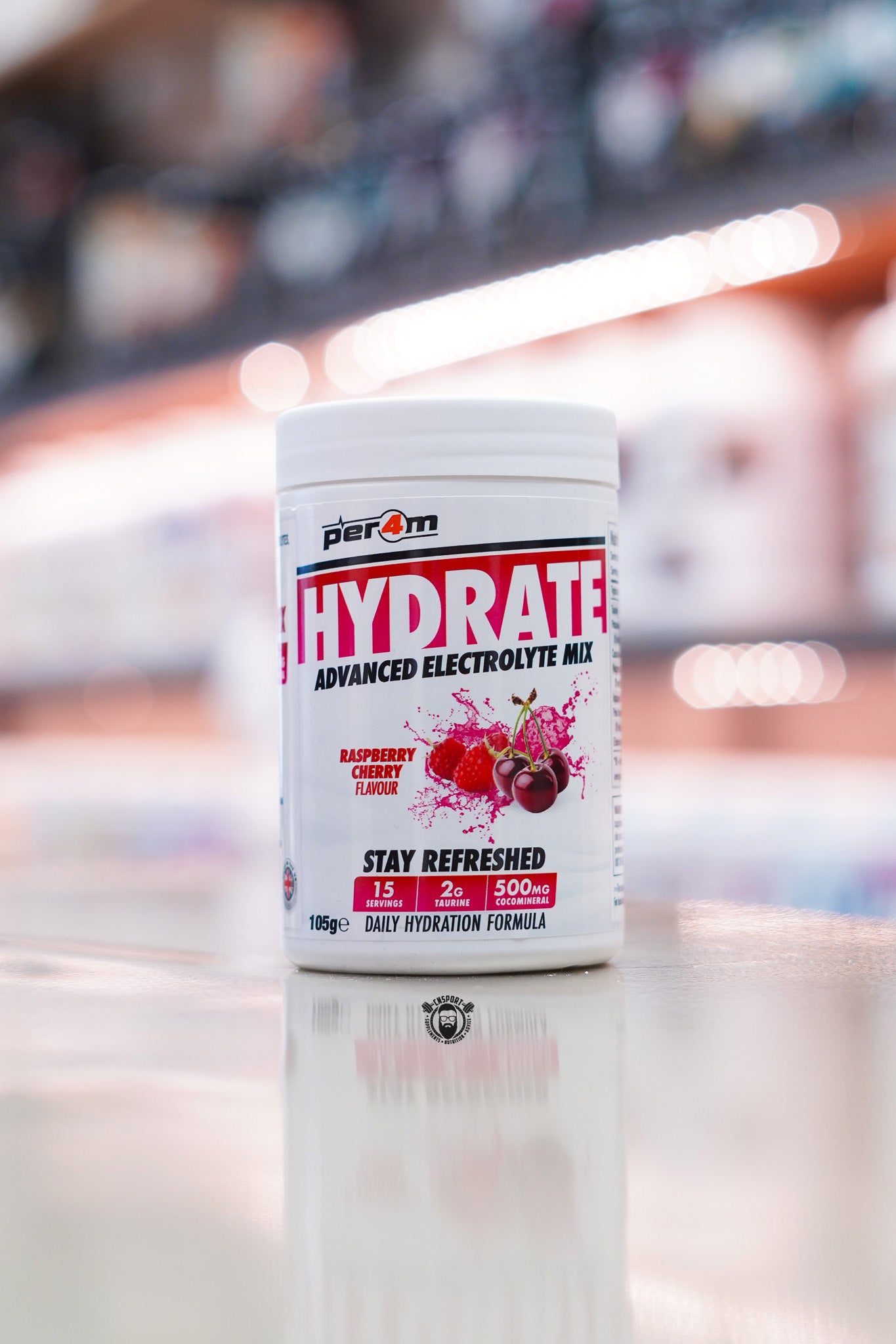 Per4m Hydrate Advanced Electrolyte Mix in Raspberry Cherry flavour, featuring 2g taurine, CocoMineral®, 15 servings and a daily hydration formula, displayed on a supplement store counter.